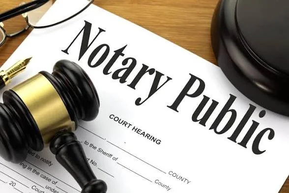 A notary public document on a wooden surface with a gavel, and a black case in the background.