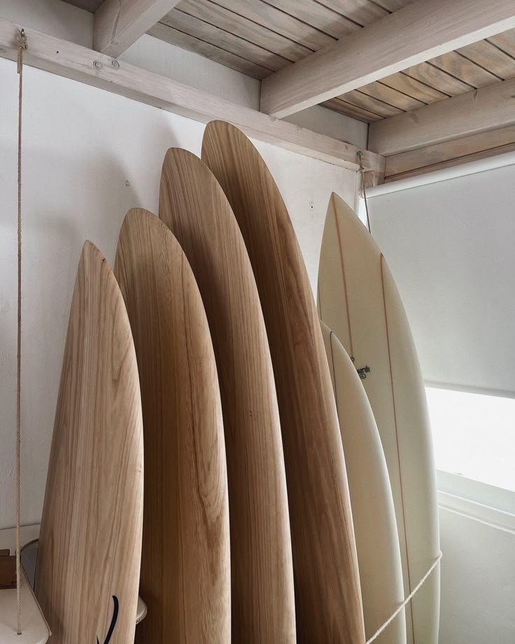 A row of wooden surfboards standing upright in a corner near a window.