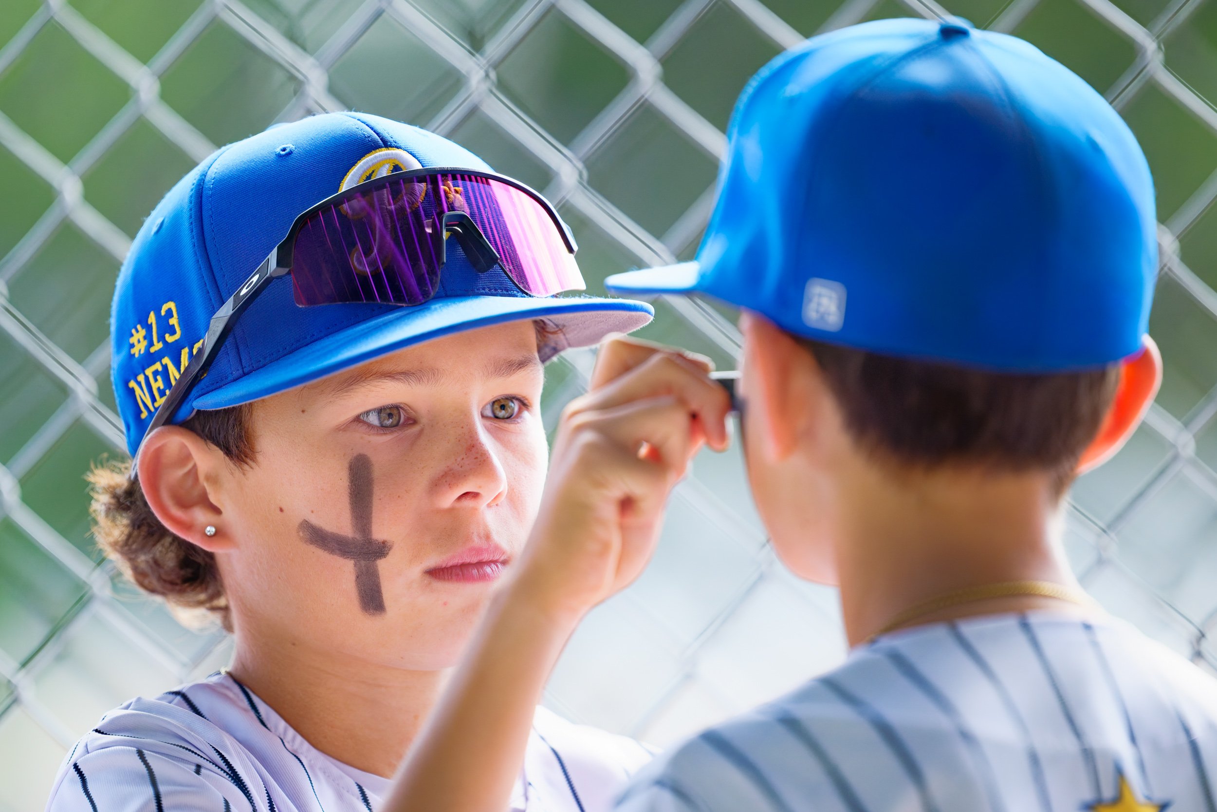 Pocket Little League U-11 All-Star player applies eye black to a teammate before a baseball game.