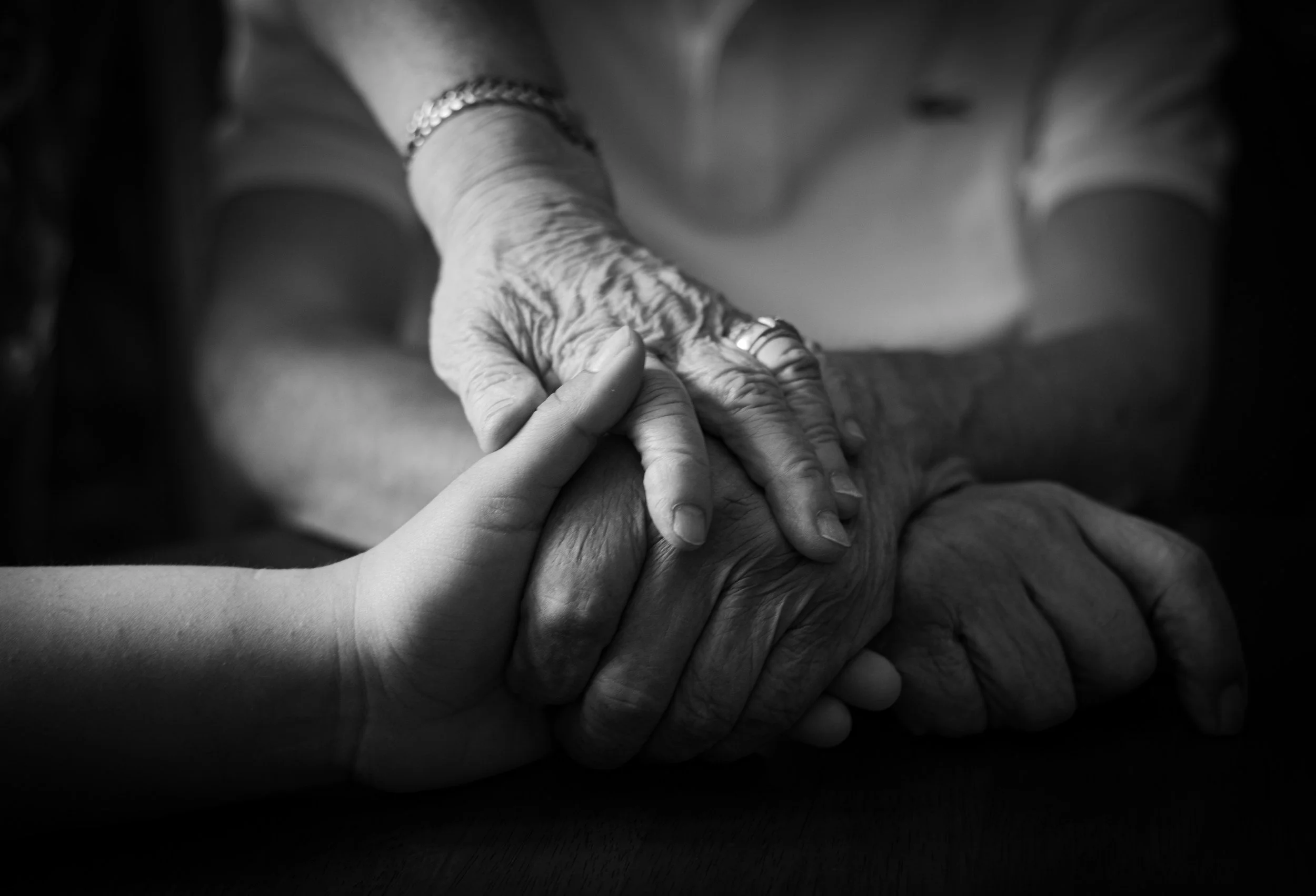 Close-up of an elderly person's hand being gently held by a younger person, in black and white.