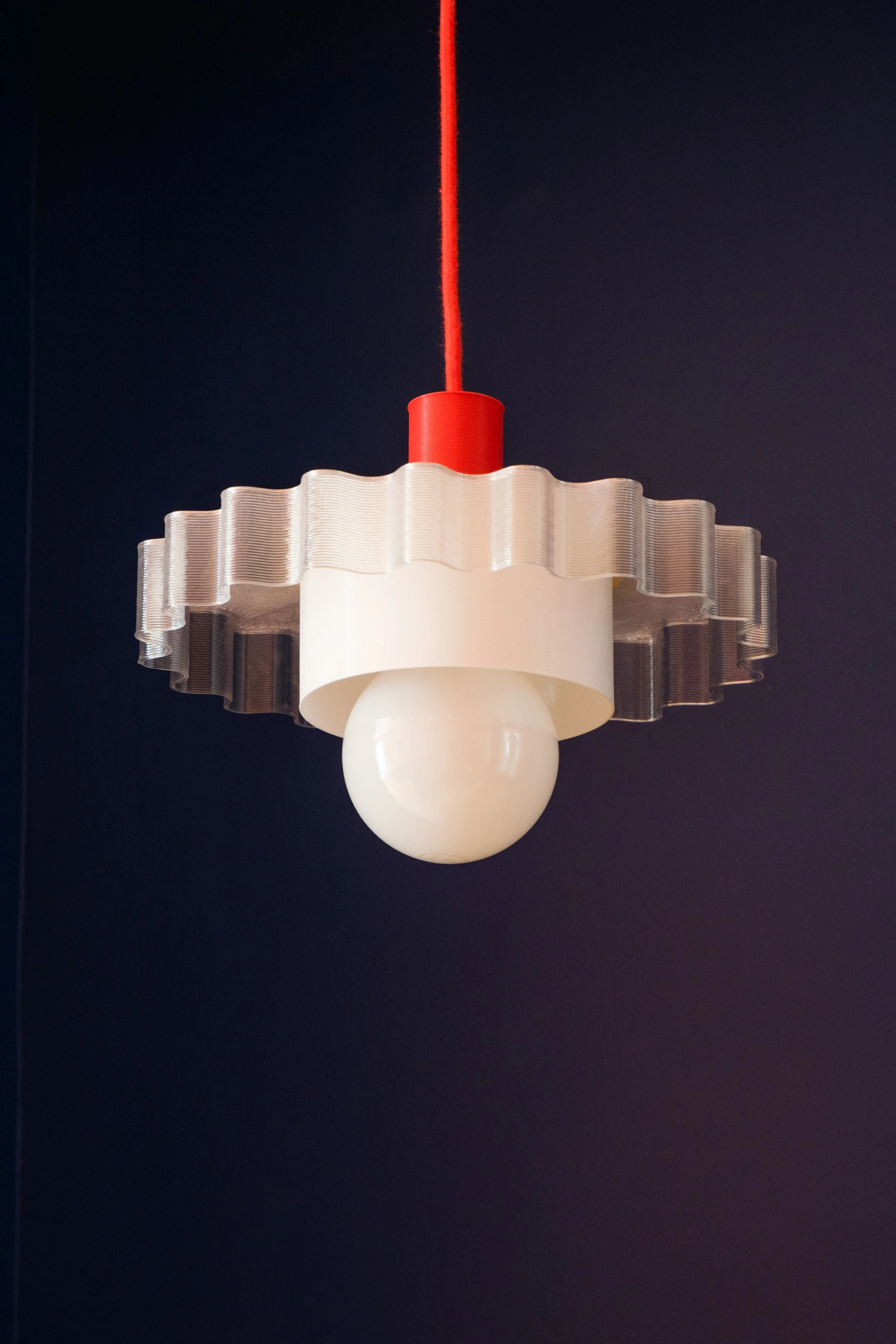 Suspension en forme de lampadaire avec un abajour en verre ondulé et une boule en verre opaque en dessous, suspendue par un câble rouge