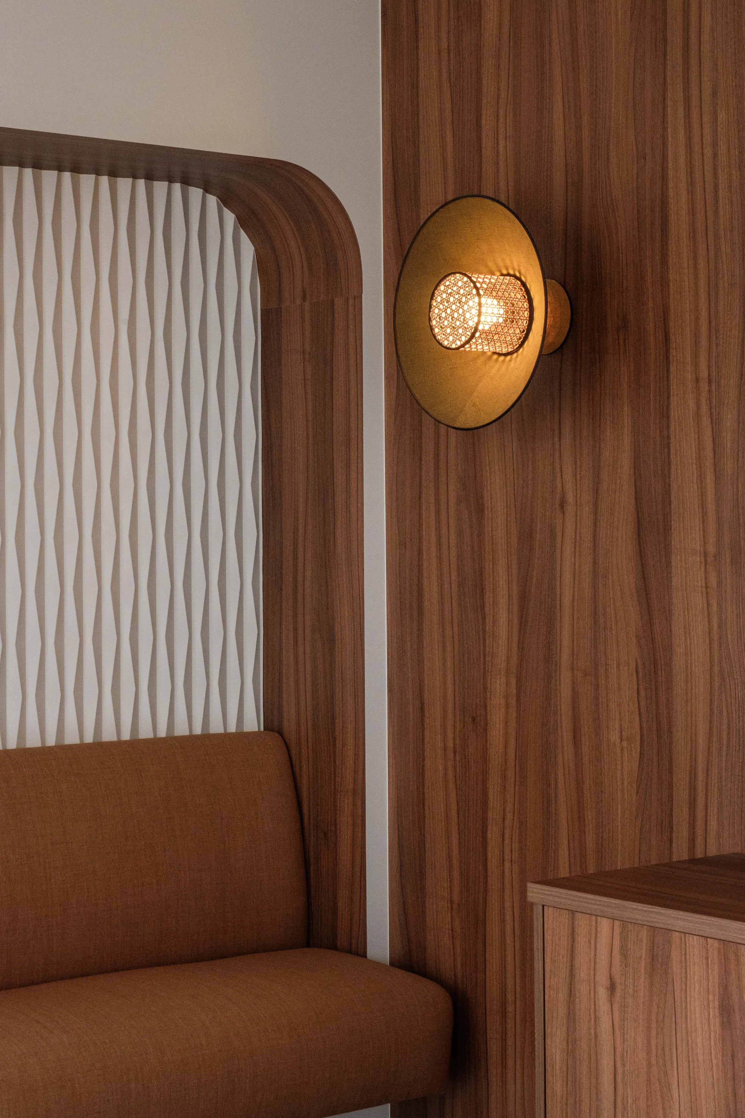 Un coin de chambre avec un mur en bois, un lampadaire suspendu avec un abat-jour jaune et un canapé marron.
