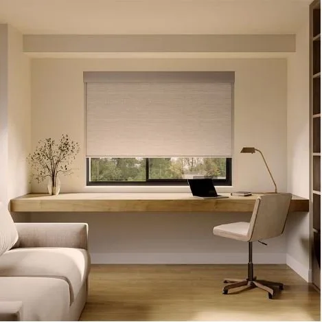 An organized home office with a large window, gray roller blind, desk with a laptop, desk lamp, chair, and a sofa on the left.