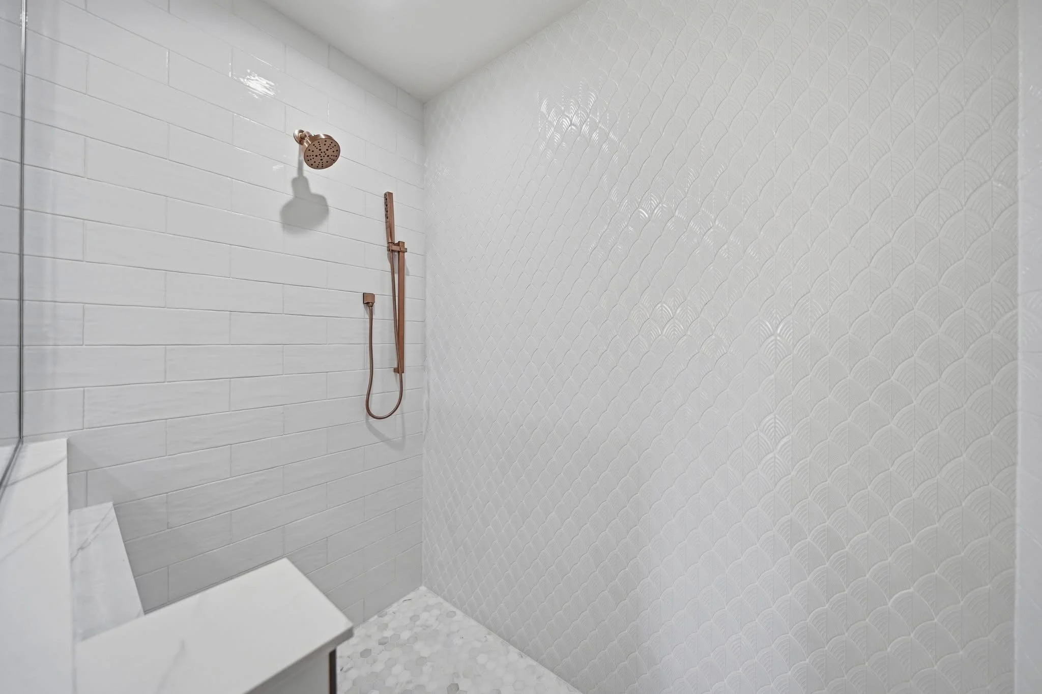 Bathroom shower with white subway tiles on the wall, a bronze showerhead, a copper handheld shower, and a small section of a vanity countertop.