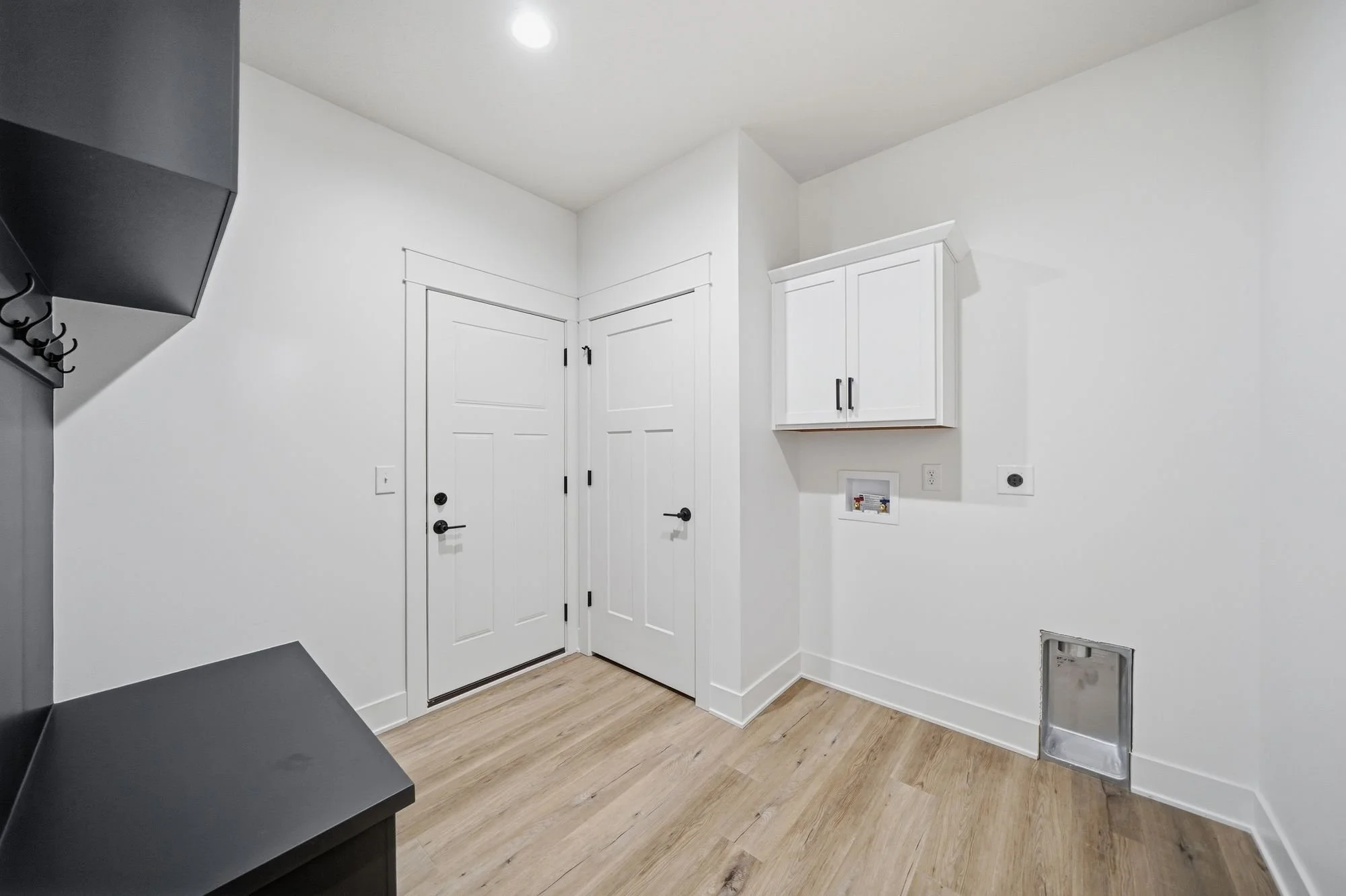 Empty laundry or utility room with white walls, a white cabinet, a door, a vent, and hookups for a washer and dryer, with wooden flooring.