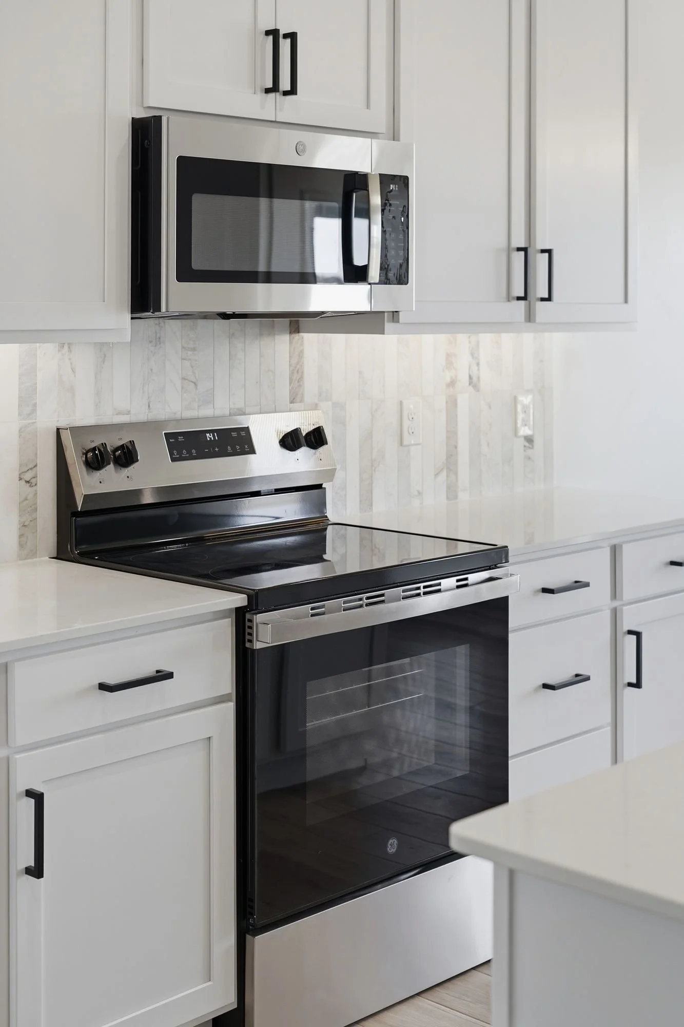 Kitchen with white cabinets, a black and stainless steel oven, and a microwave installed above the stove.