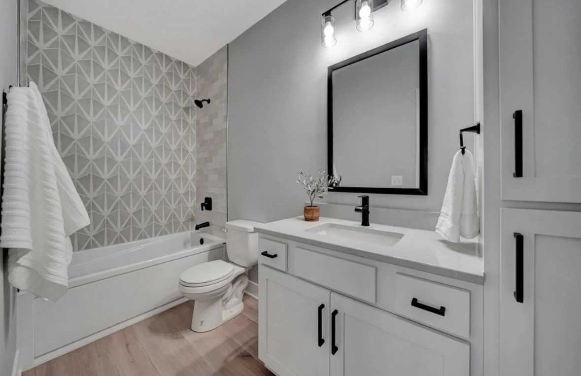 Modern bathroom with a bathtub, toilet, and vanity with a sink, mirror, and cabinets in neutral colors.