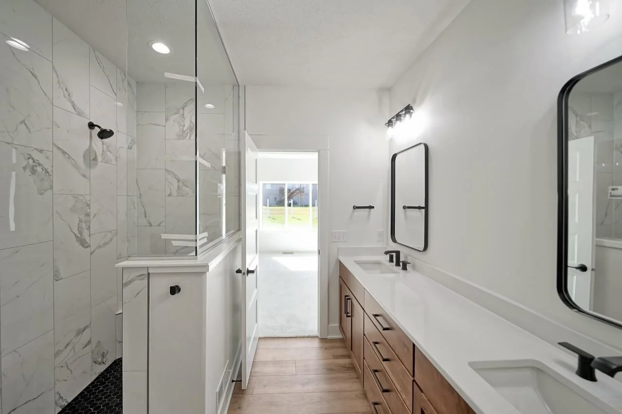Modern bathroom with double sink vanity, black-framed mirrors, and a separate glass-enclosed shower with marble walls.