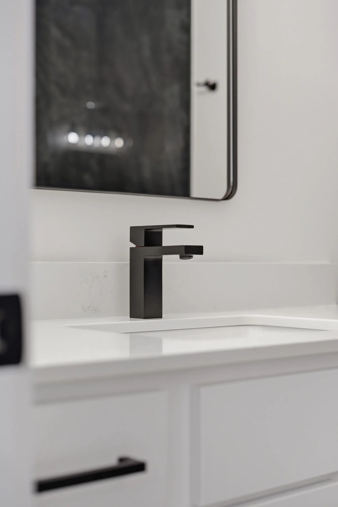 Close-up of a modern black faucet on a white bathroom sink with a mirror in the background.