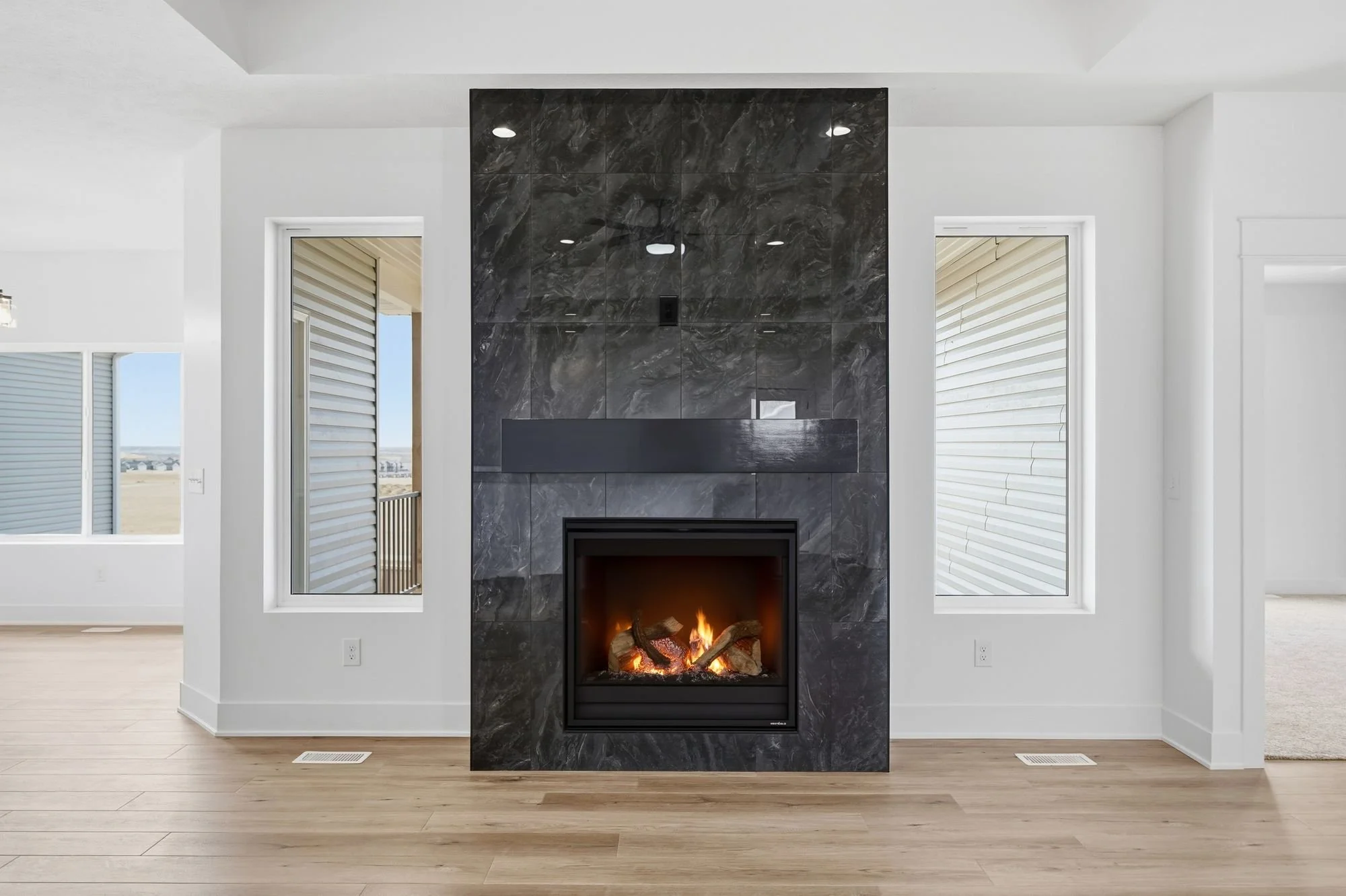 Modern living room with a black marble fireplace, white walls, two windows, and wood flooring.