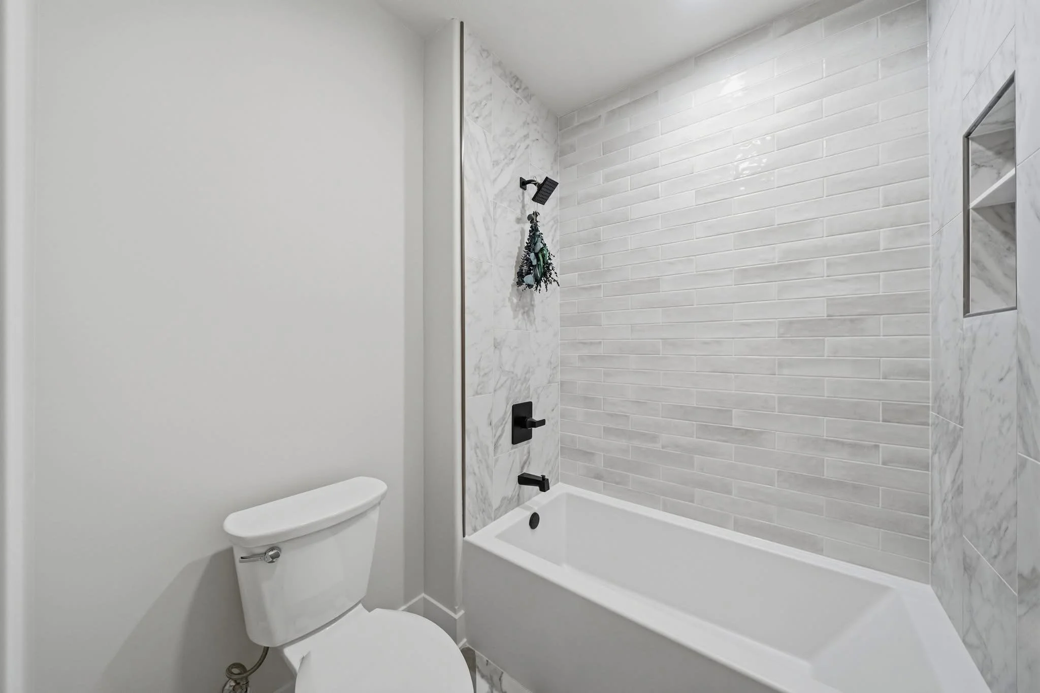 Modern bathroom with white walls, marble and tile accents, a bathtub with a rainfall showerhead, a toilet, and a mirrored wall cabinet.