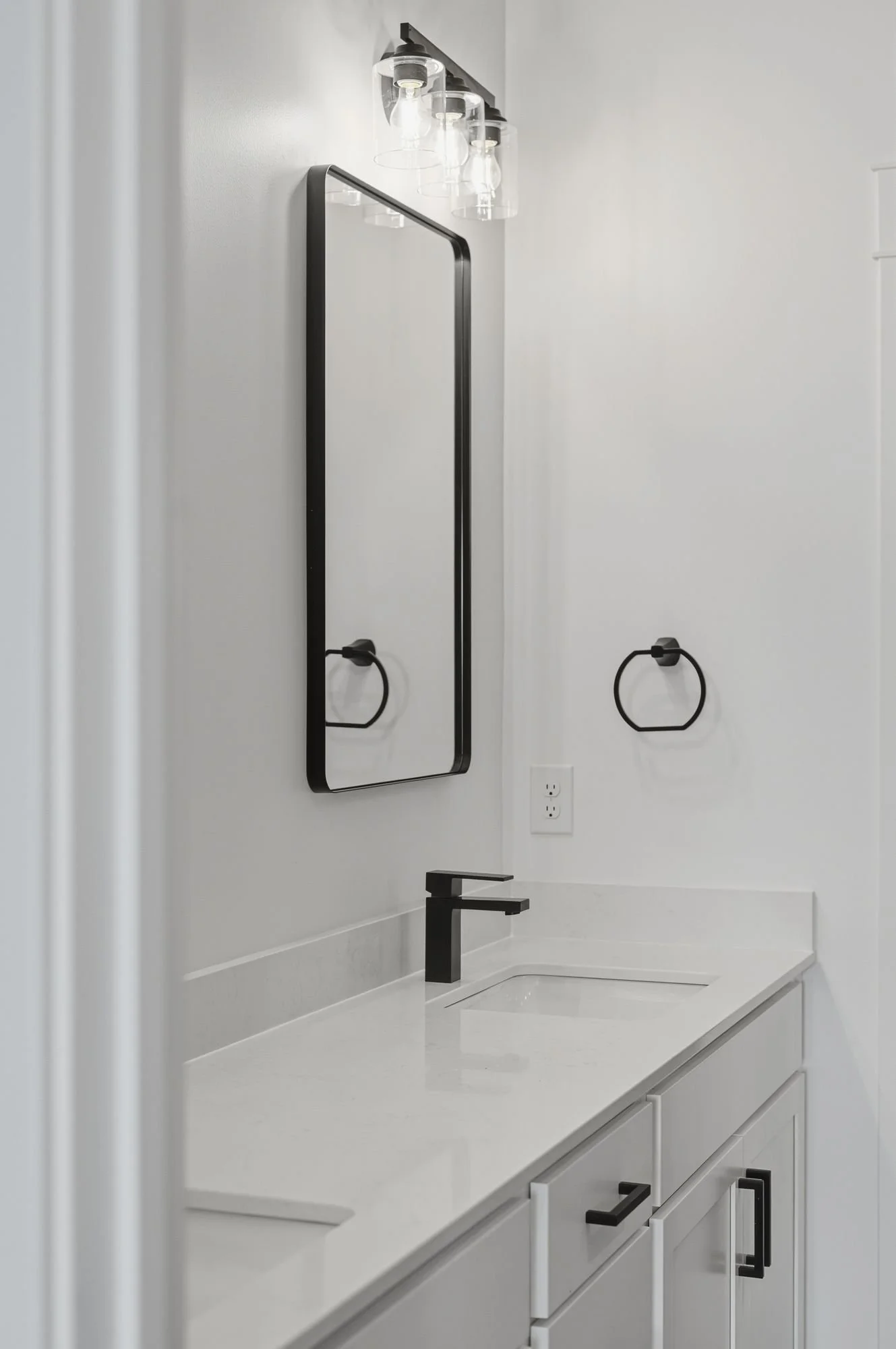 Modern bathroom vanity with white countertop, black faucet, wall-mounted mirror, and glass light fixture with four bulbs.