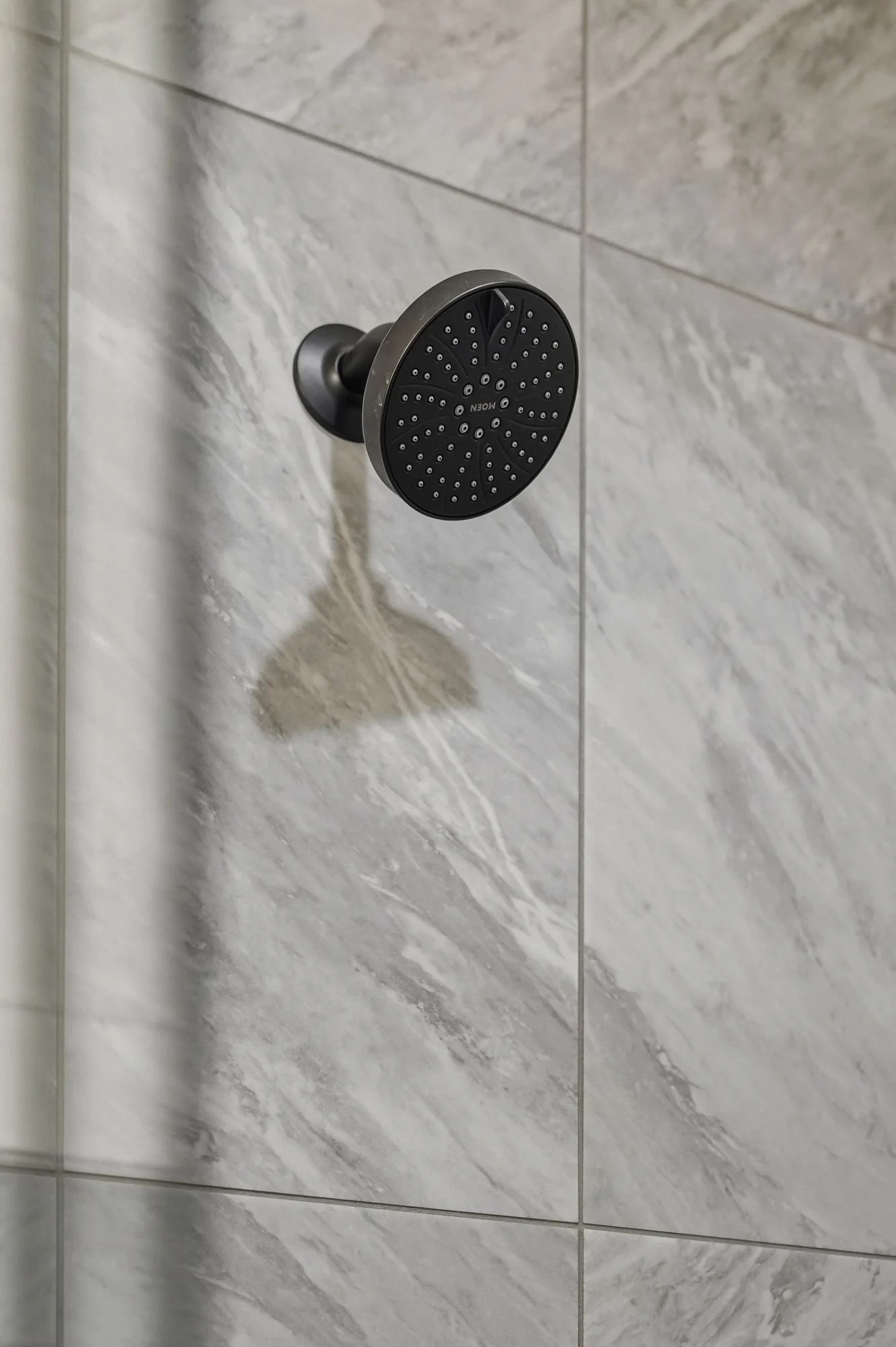 A black and silver showerhead mounted on a gray marble tiled wall in a shower.