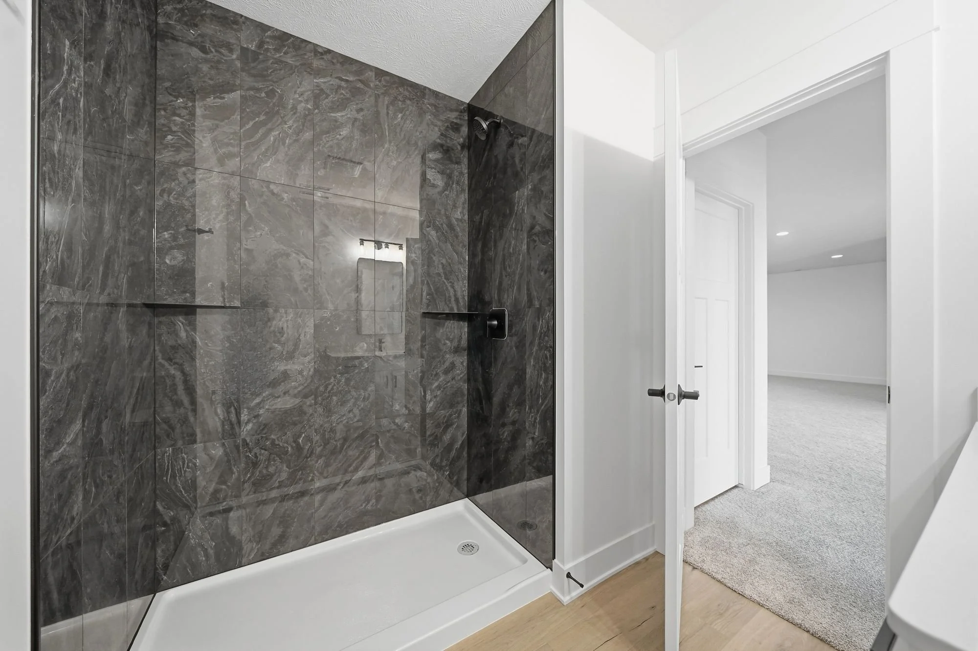 Modern shower with dark gray marble tiles, white shower base, glass door, and a showerhead.