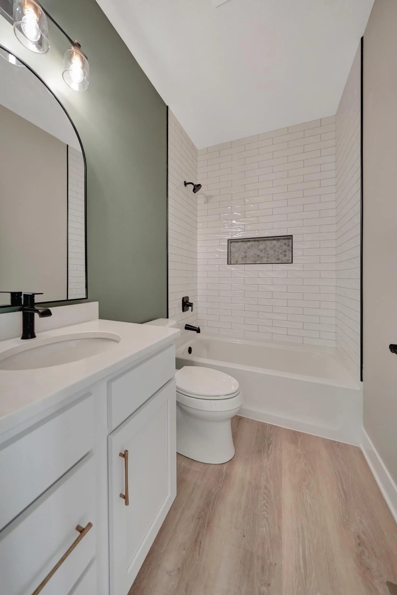 Modern bathroom with white vanity, black faucet, toilet, bathtub, and tiled shower area with built-in niche