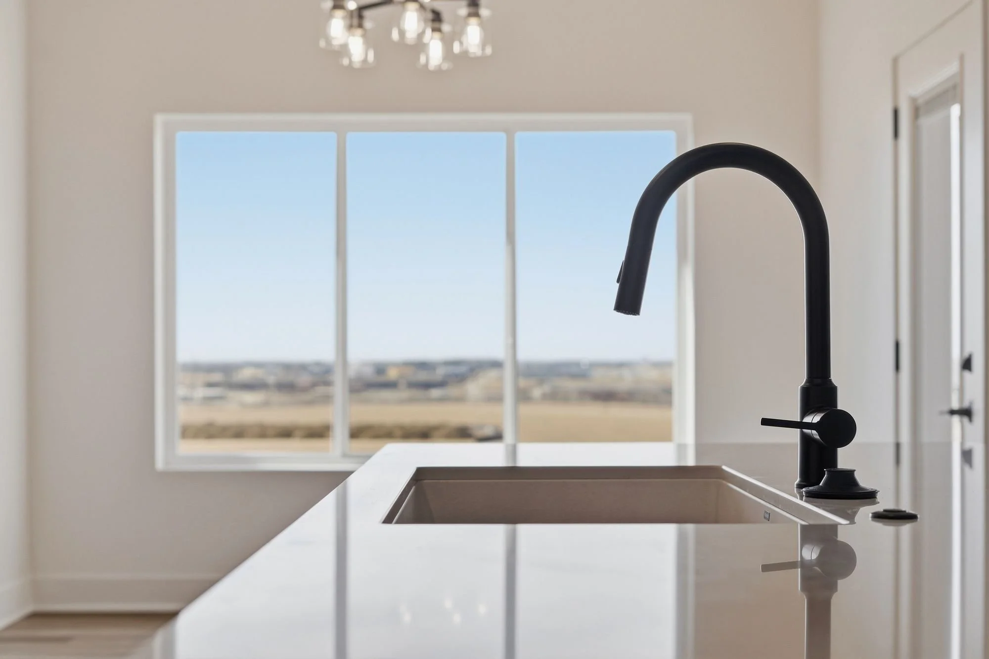 Modern kitchen with black faucet over white sink, large window showing landscape outside, minimalistic design.