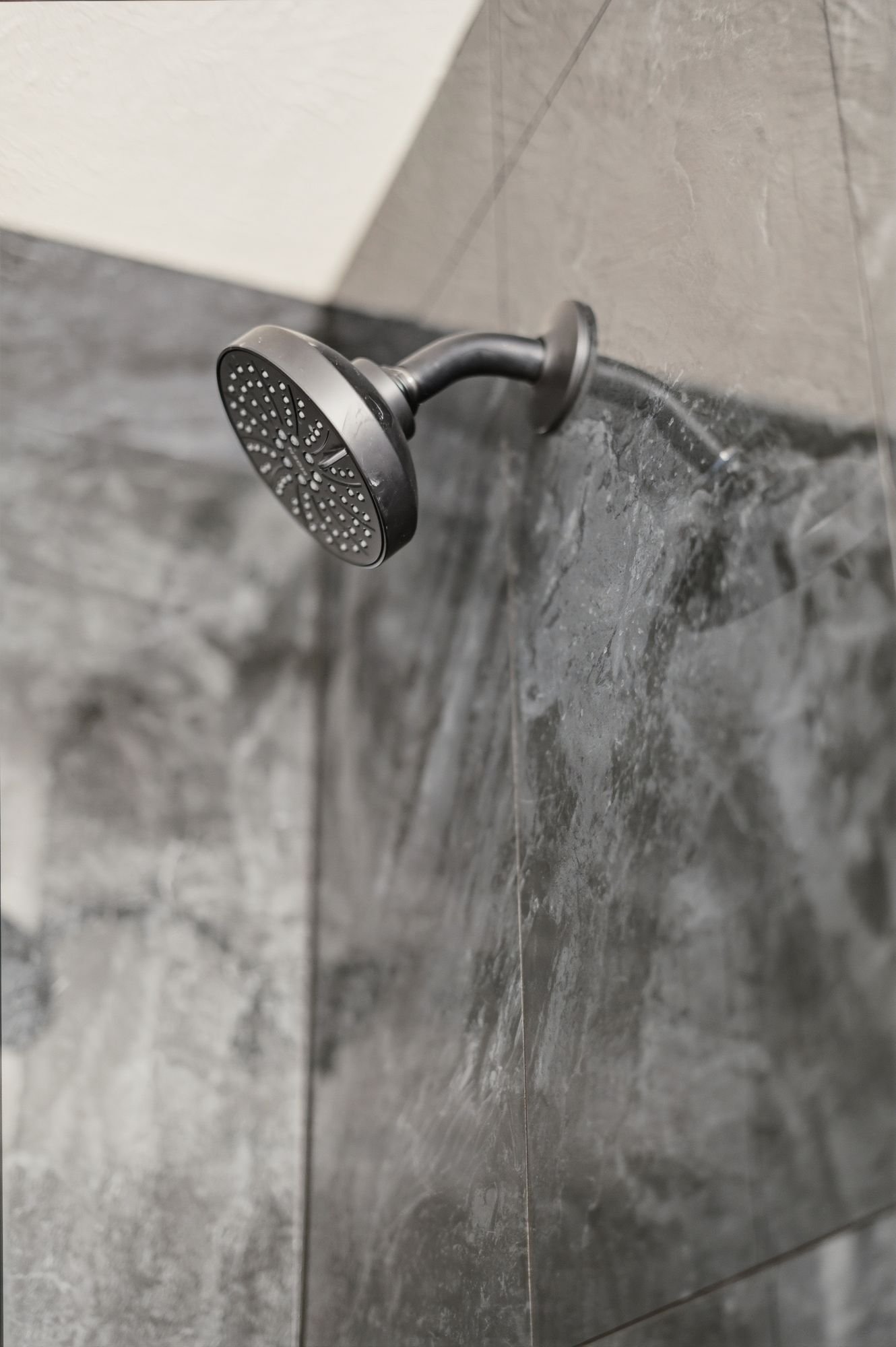 Close-up of a black handheld showerhead mounted on a bathroom wall with gray tiles.