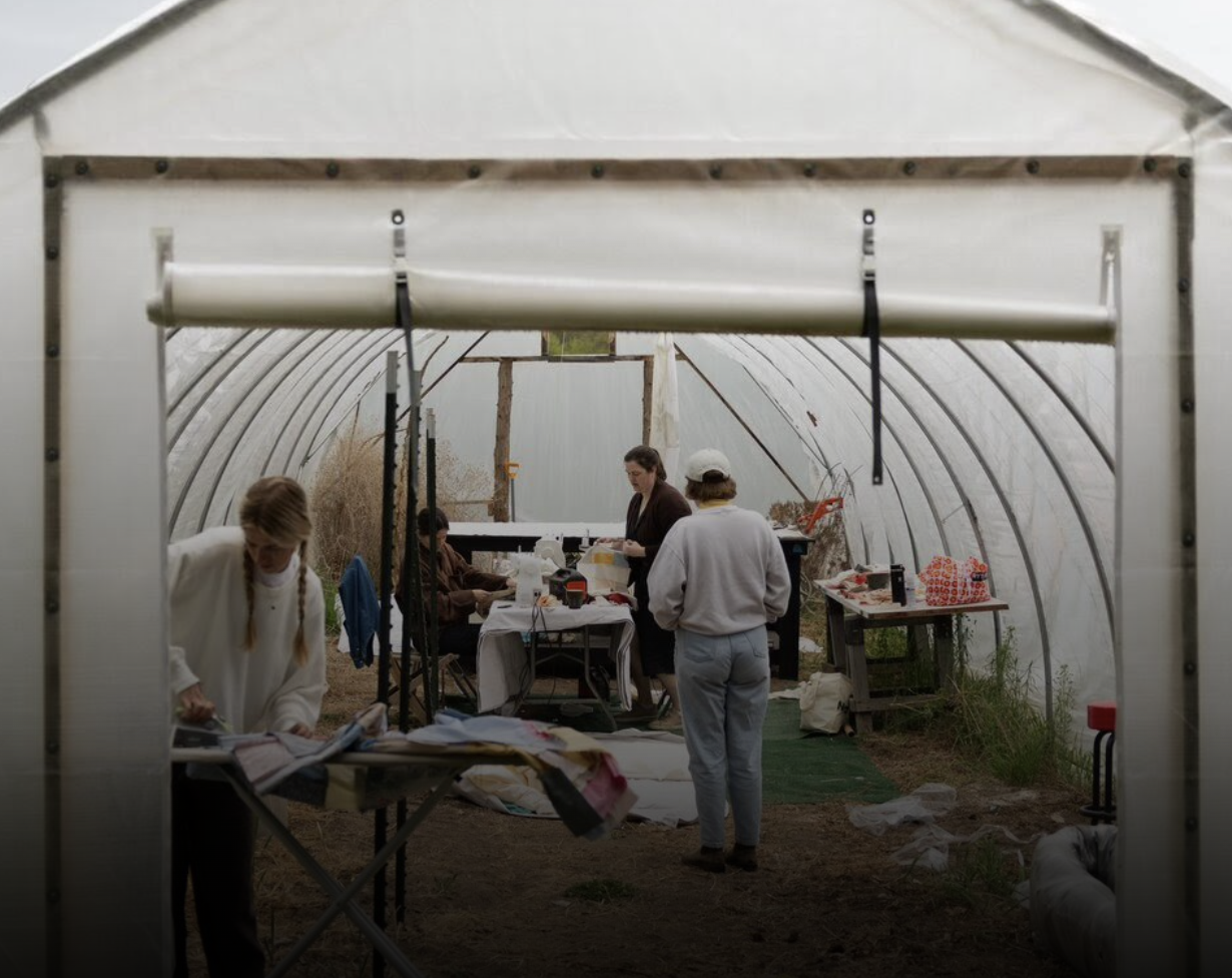 People working inside a greenhouse, with tables and equipment, preparing for a project or activity.