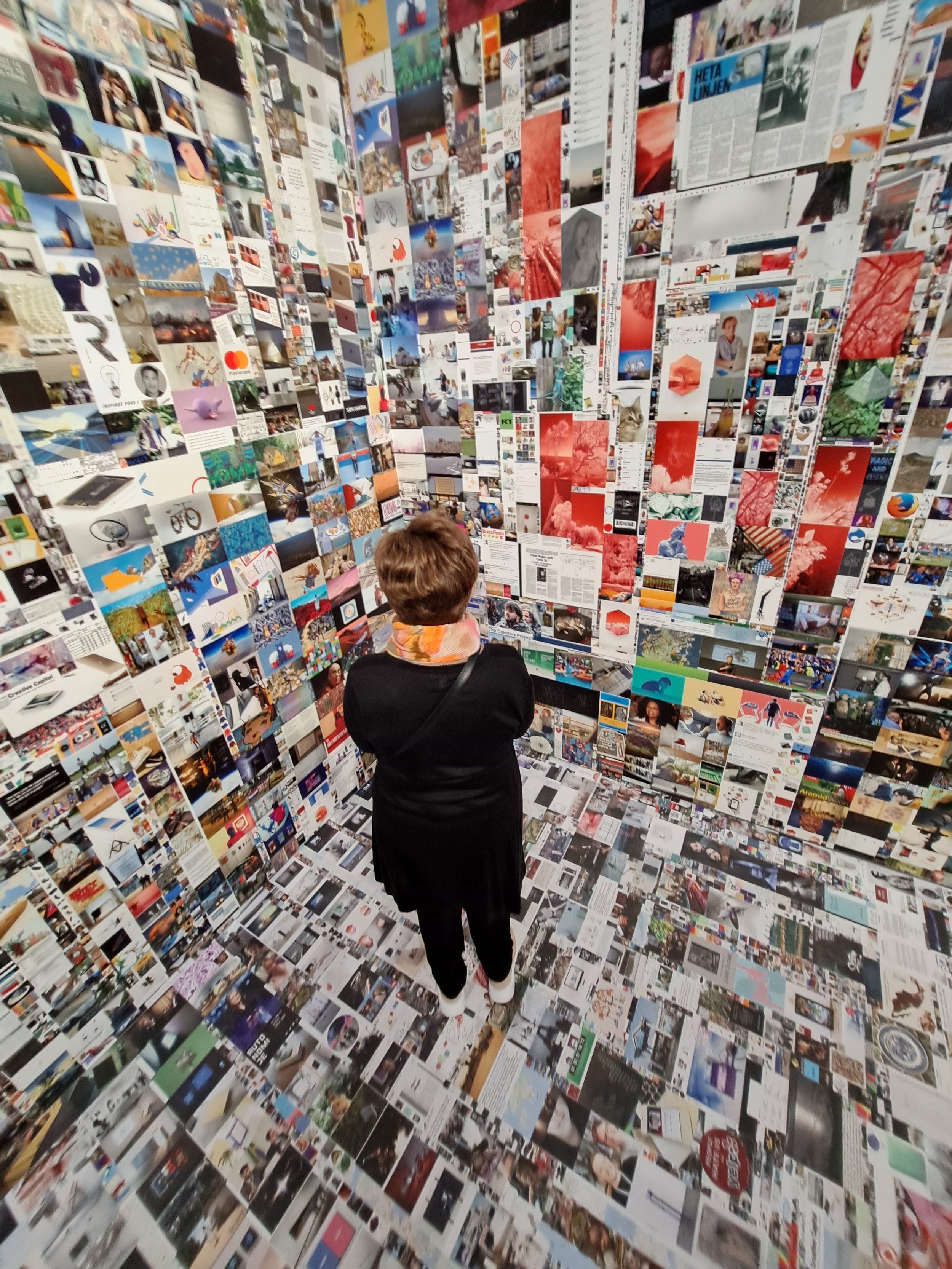 Ein Besucher betrachtet eine Wand aus unzähligen Fotos und Artikeln in einer Kunstausstellung.