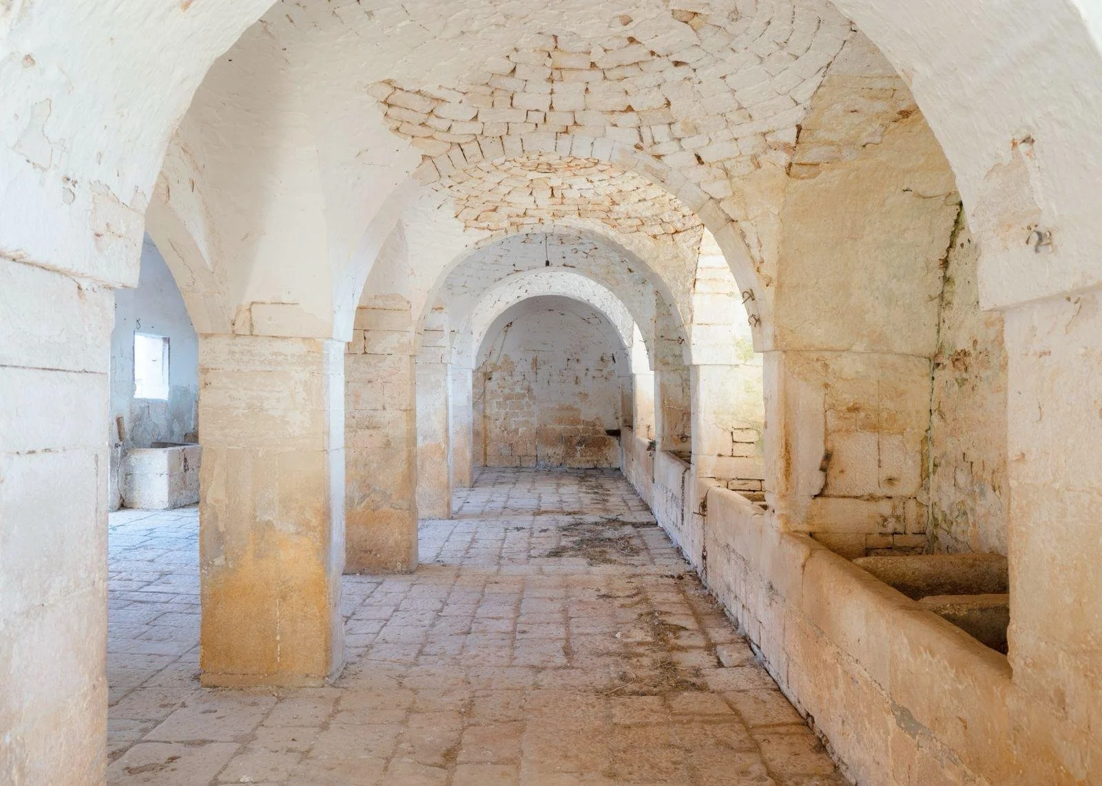 Old stone corridor with arched ceilings and stone sinks along one side.