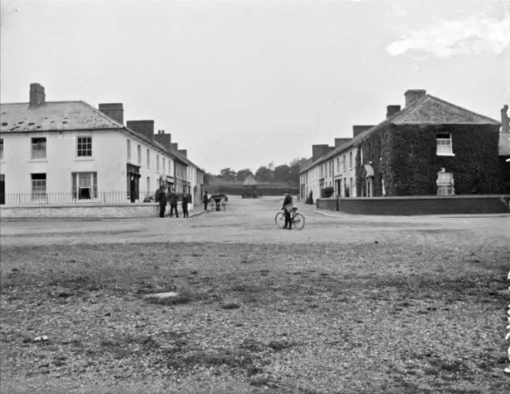 Black and white historical photo of a street scene with old buildings, a bicycle rider, and a few pedestrians.