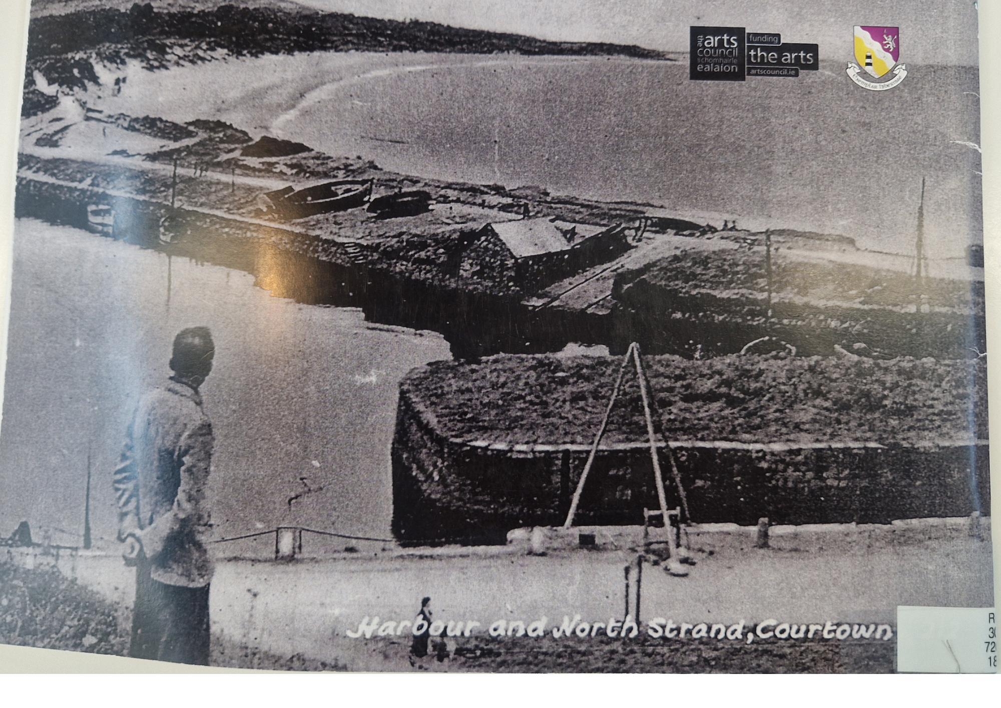 A vintage black-and-white photograph of Harbour and North Strand in Courtown, showing a seascape with boats on the beach, a man standing near the shoreline, and several trees and utility poles in the background. There are stickers in the top right co