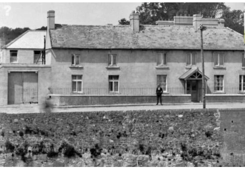 Black and white photograph of a large, two-story brick house with multiple chimneys and a man standing outside near the front entrance.