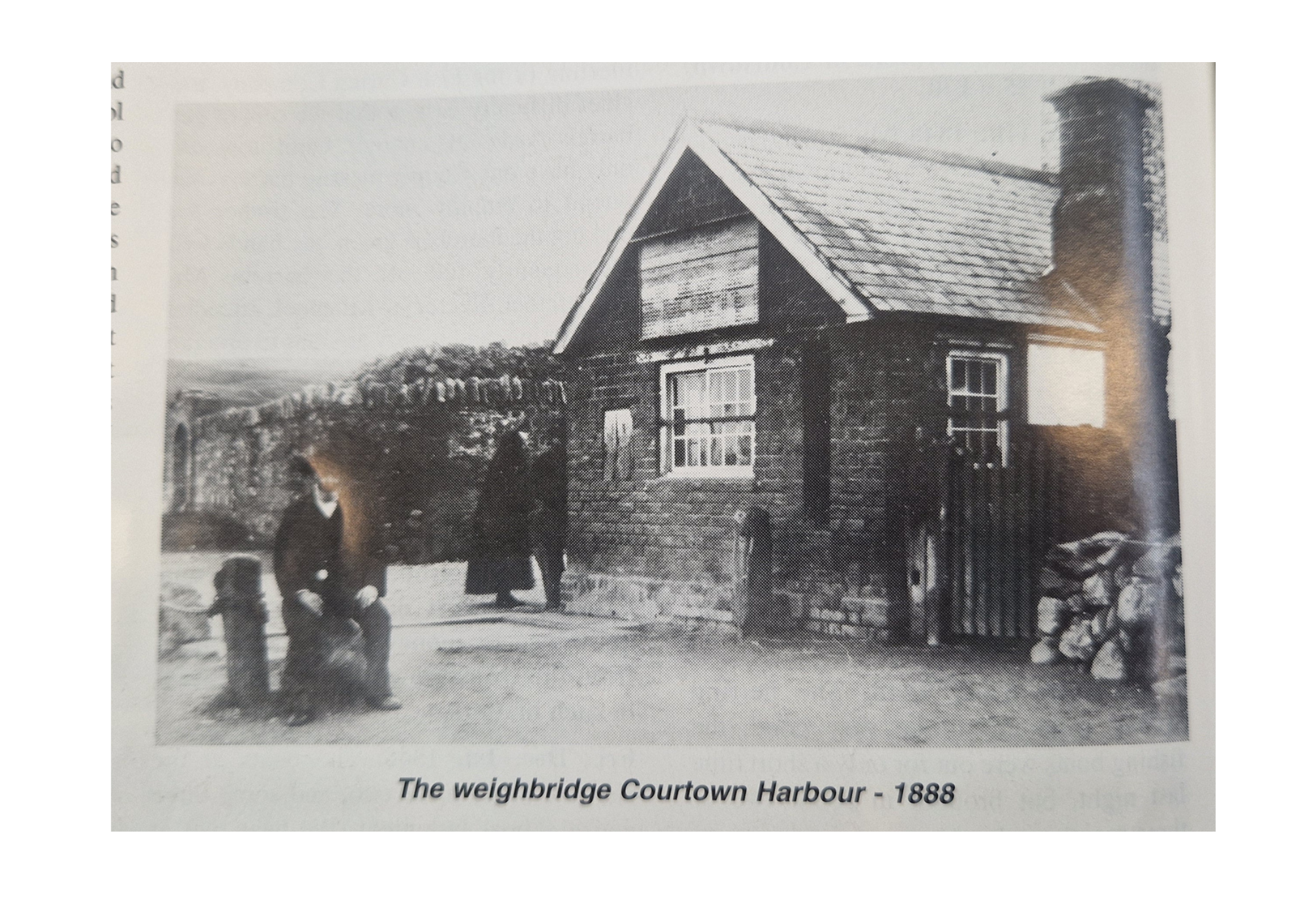 Black and white photograph of a two-story stone building with a sloped roof and a chimney, labeled as The weighbridge Courtown Harbour from 1888. Three men are sitting and standing in front of the building, with a background of hills and trees.