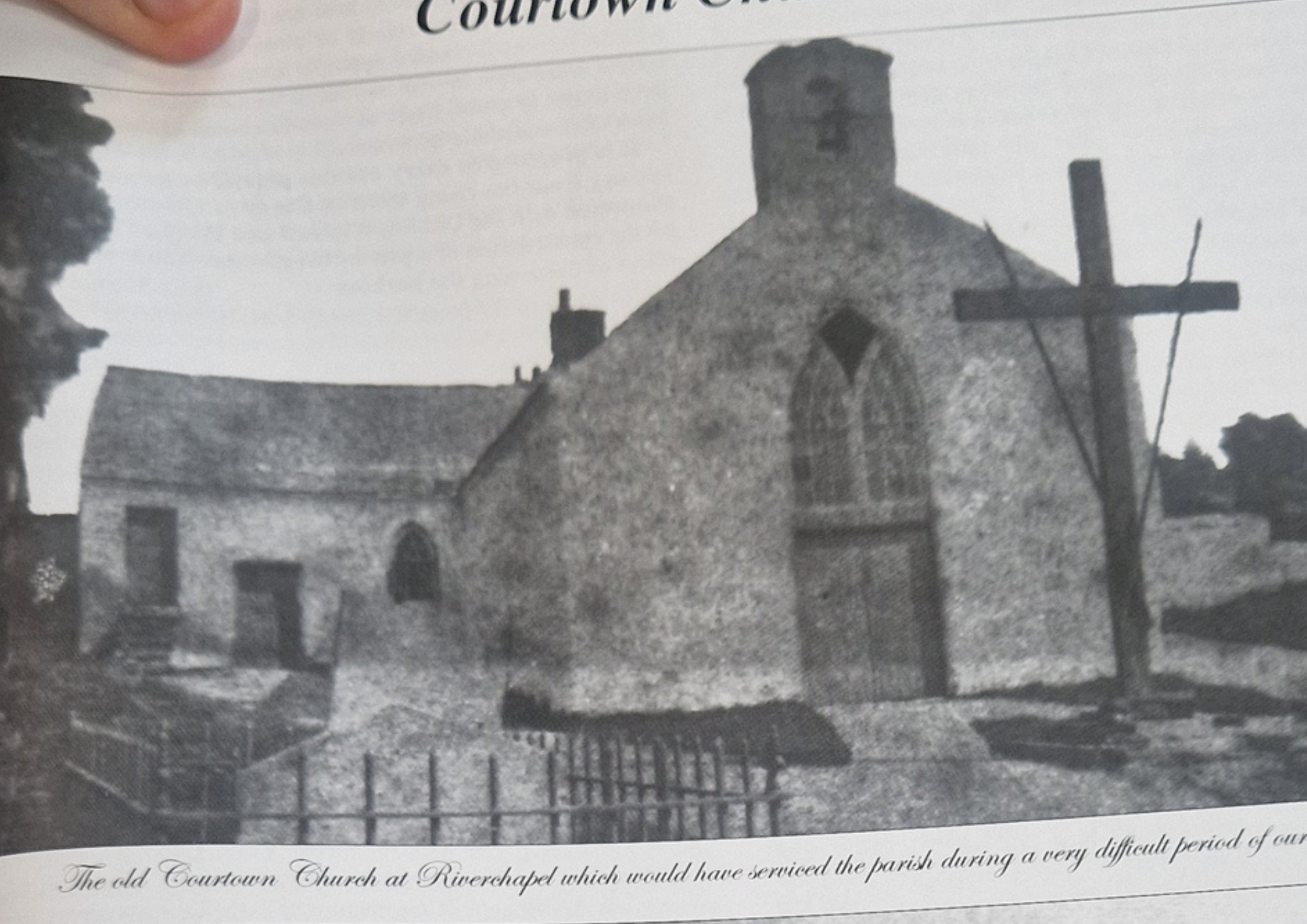 Black and white photo of an old church with a stone façade, arched doorways, a tower, and a fence in front.