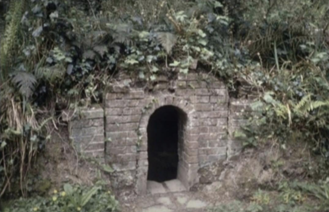 Small brick structure with a rounded doorway, nestled in a lush, green forest.