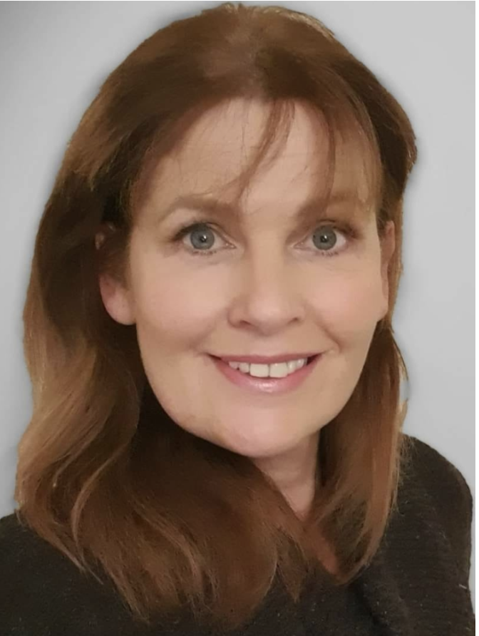 A woman with shoulder-length reddish-brown hair, blue eyes, and a friendly smile, wearing a dark top.