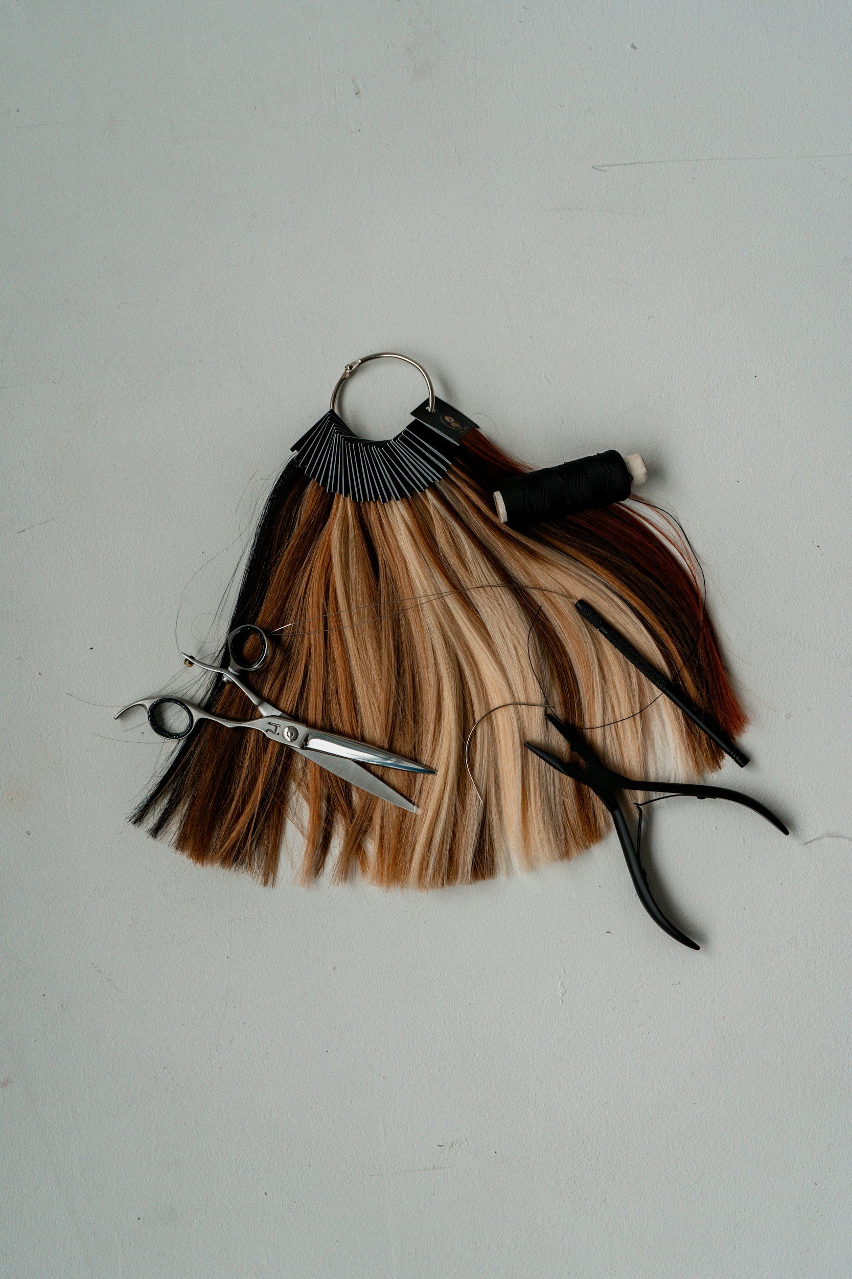 Array of hair styling tools including scissors, a comb, hair clips, hair dye, a hairpin, and a hair color swatch, arranged on a plain surface.