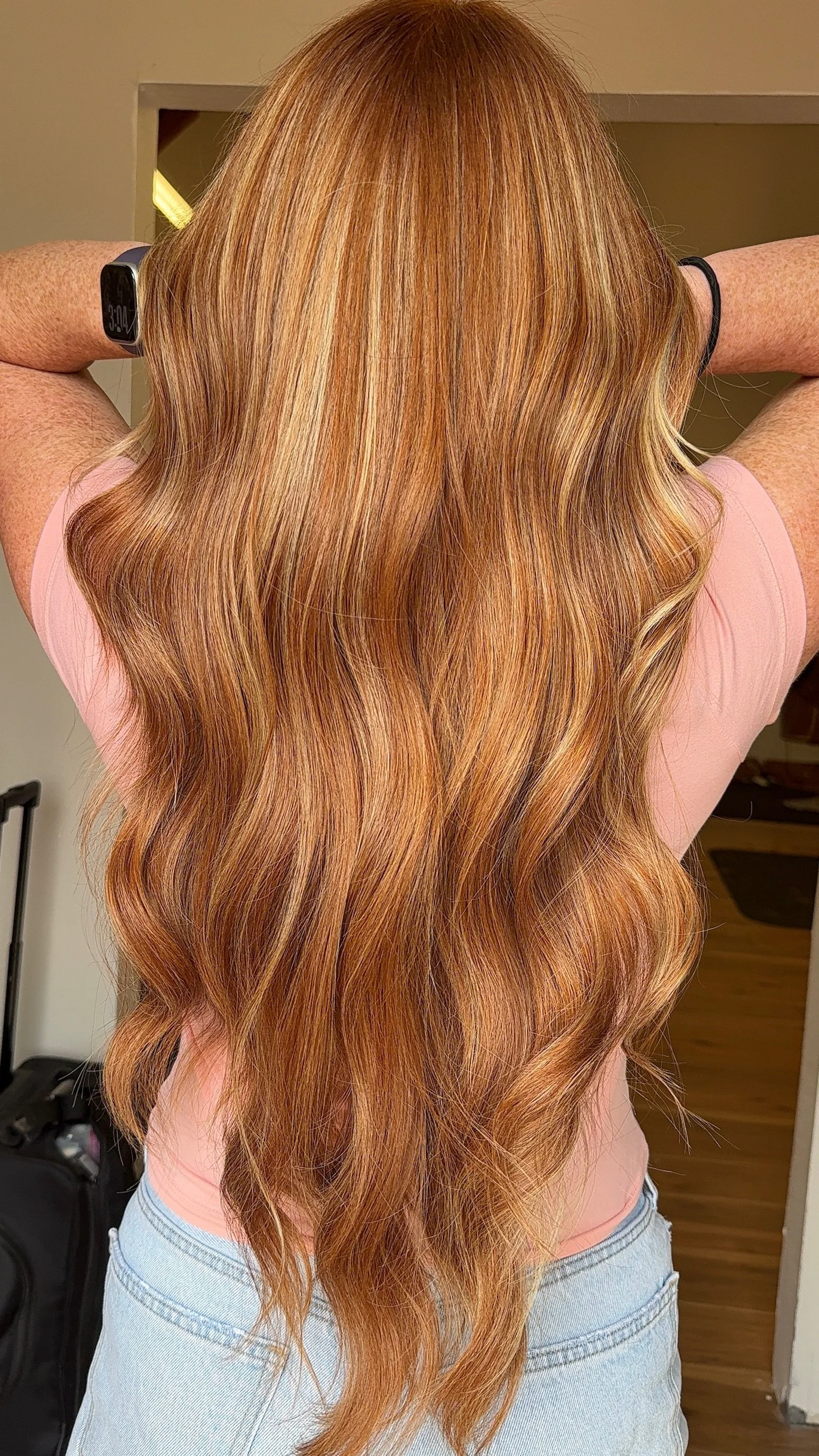 Back of a woman with long wavy brown hair wearing a cream-colored sweater.