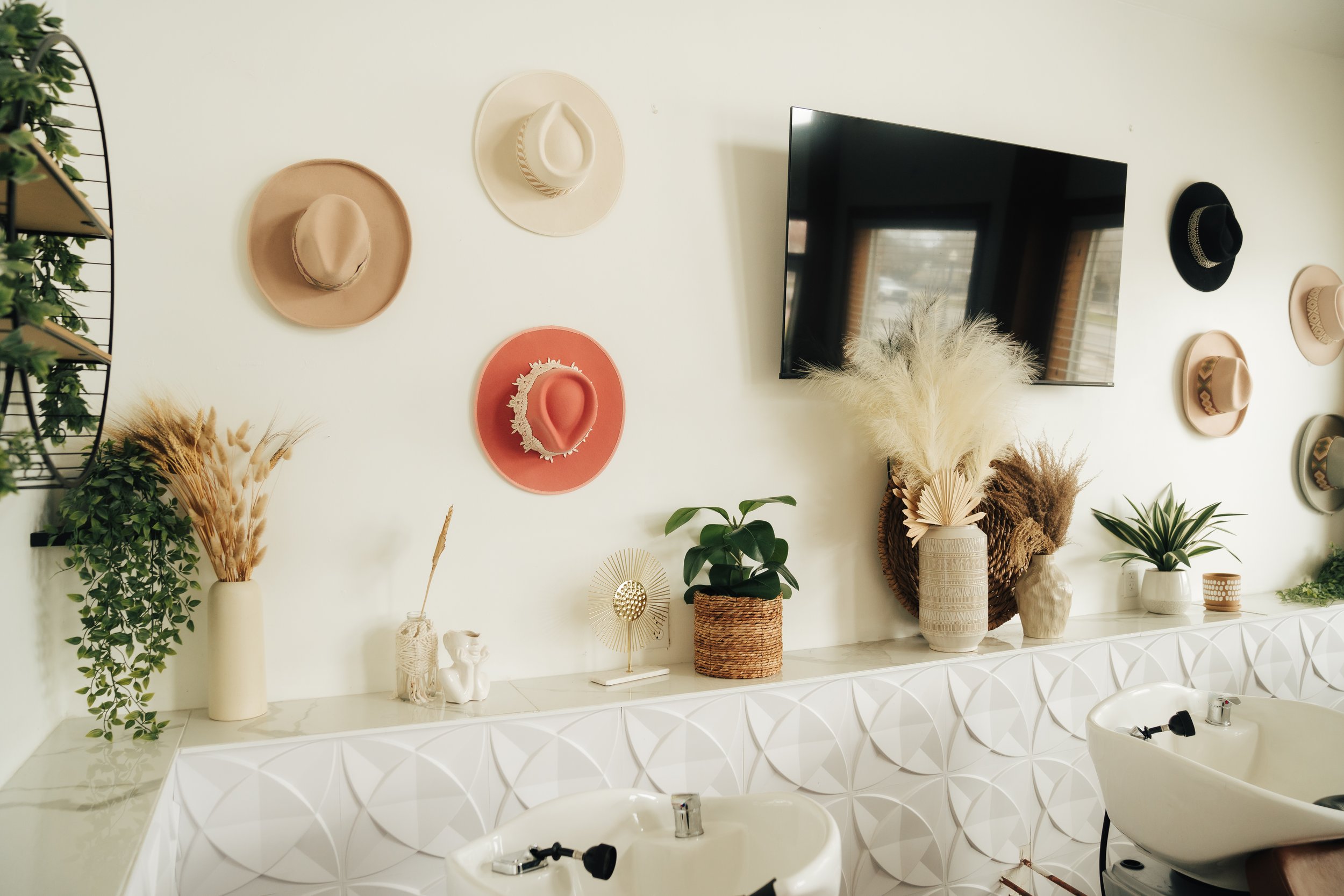 Bathroom with beige and black hats on wall, plants, and decorative items on white countertop.