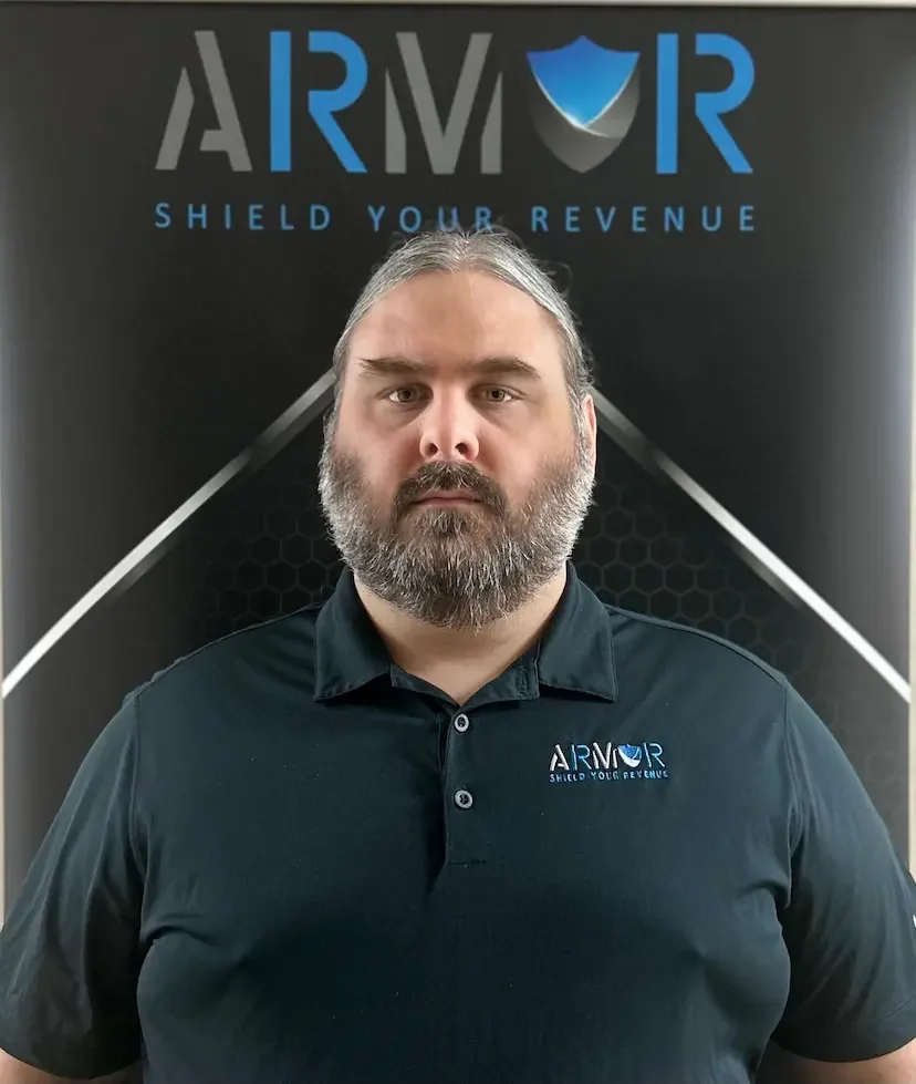 A man with a beard and long hair wearing a black polo shirt (Dustin Painter) with the Armor logo stands in front of a black backdrop with the Armor logo and the tagline "Shield Your Revenue."
