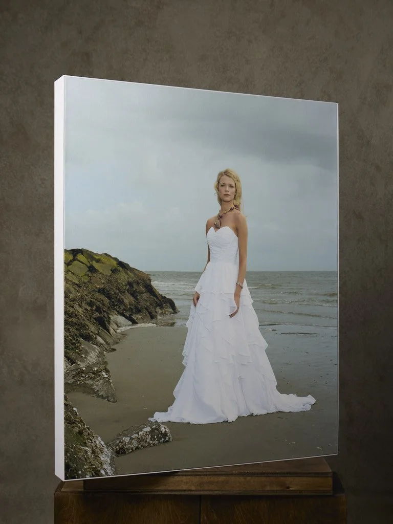 A large canvas print of a woman in a white wedding dress standing on a beach with rocks and the ocean in the background.