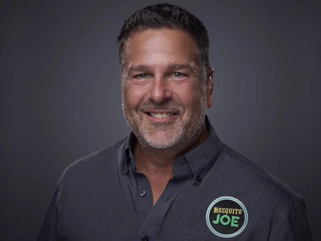 Professional headshot of a smiling man with gray hair and beard, wearing a dark gray shirt with a "Mosquito Joe" logo patch.