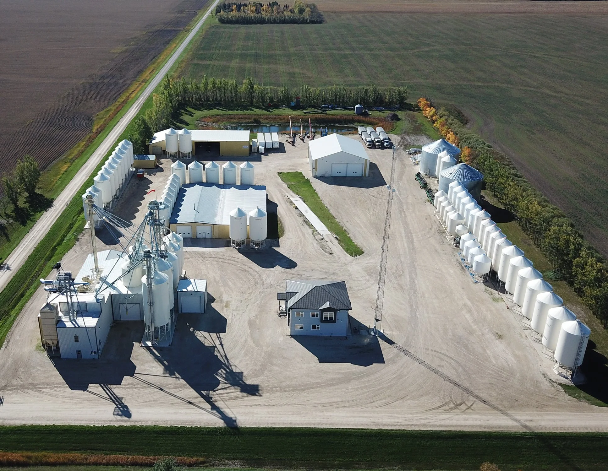 Aerial view of a farm with silo storage, a pond, and fields in the background.