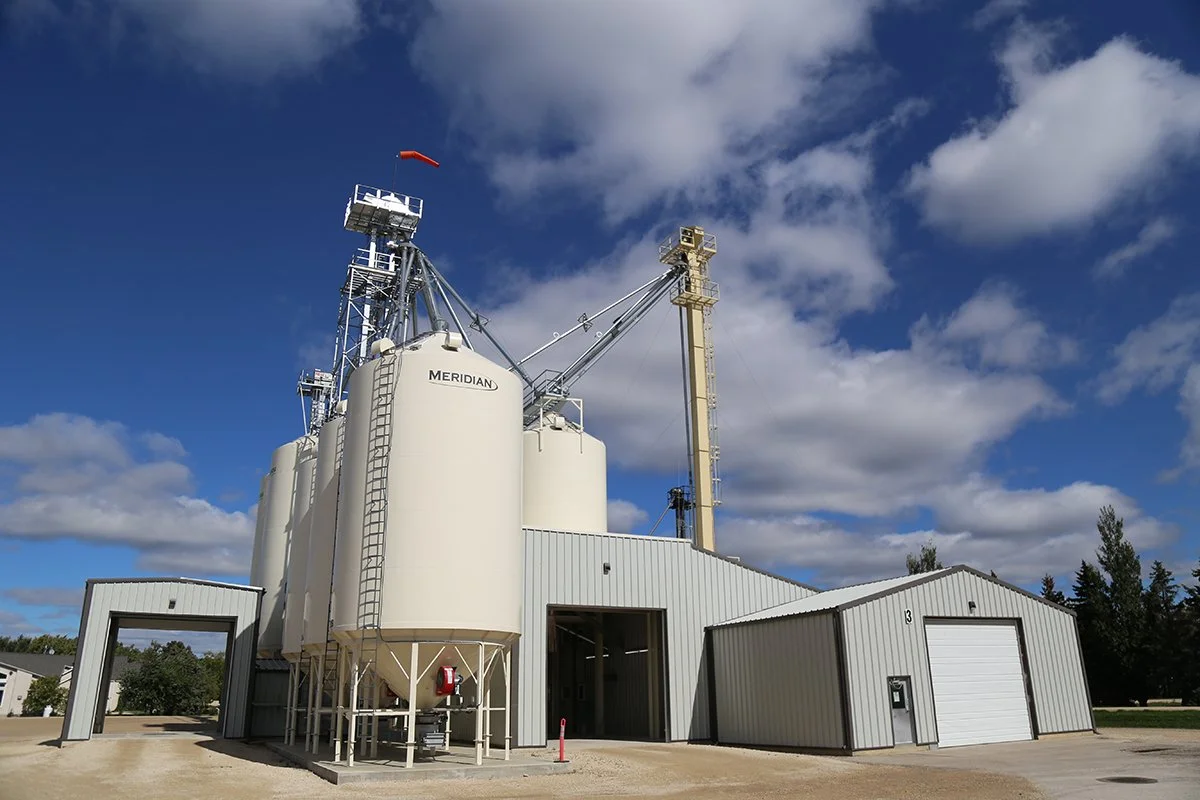 Industrial grain storage with silos and metal building under a partly cloudy sky.