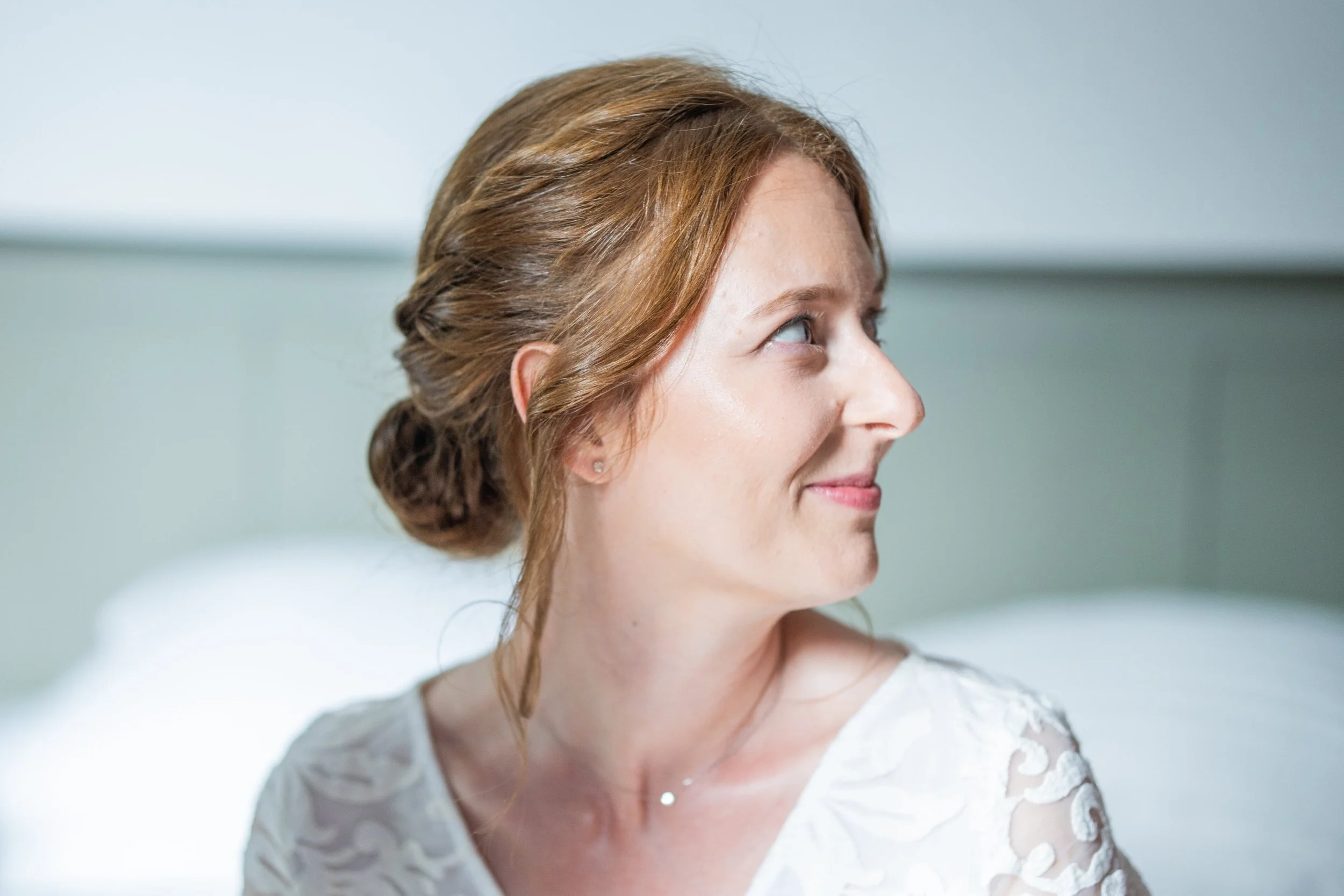 Une femme aux cheveux roux, portant une robe blanche en dentelle, regarde sur le côté.