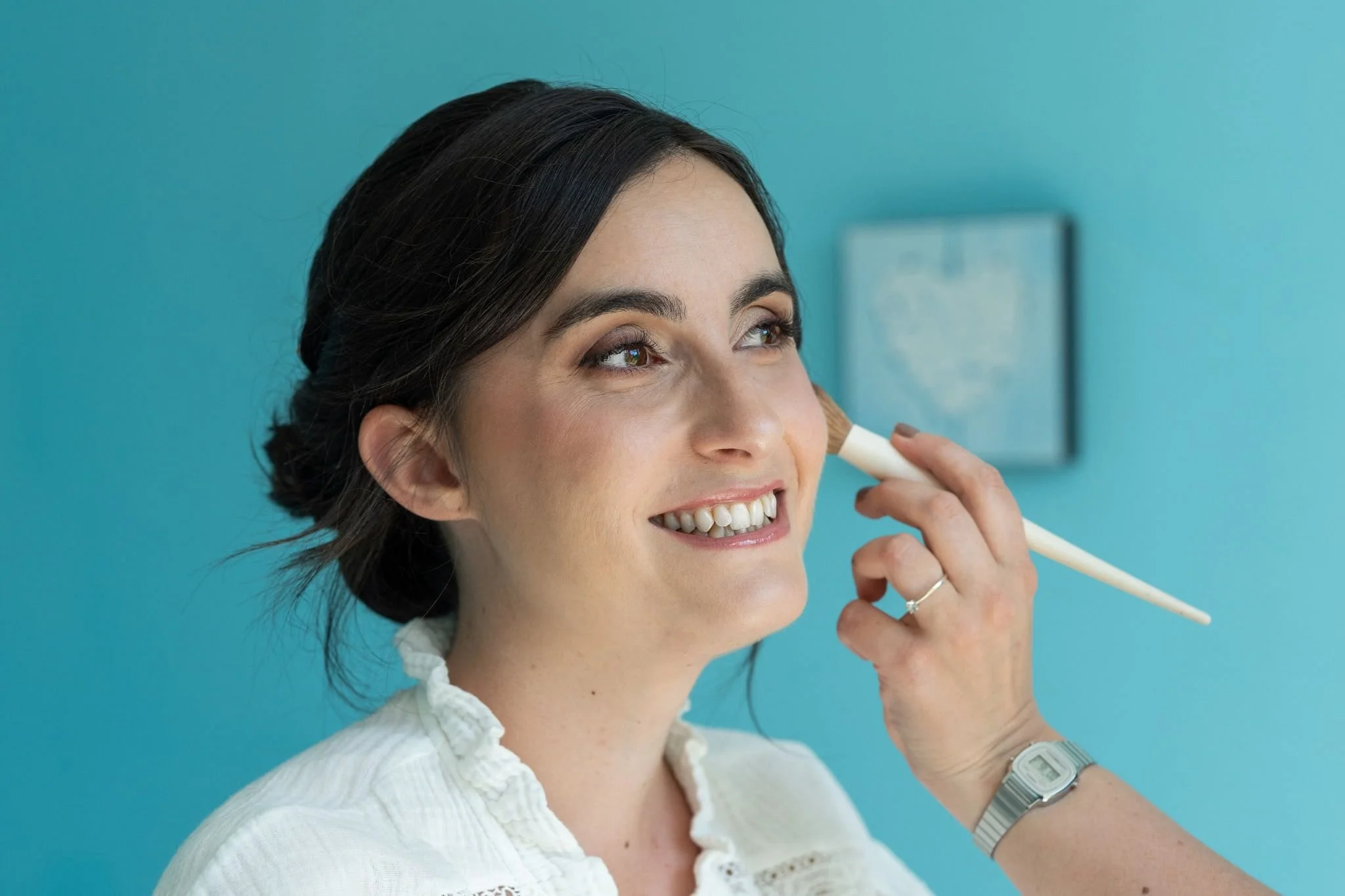Une femme souriante ajuste ses écouteurs en utilisant un stylo contre un mur bleu.