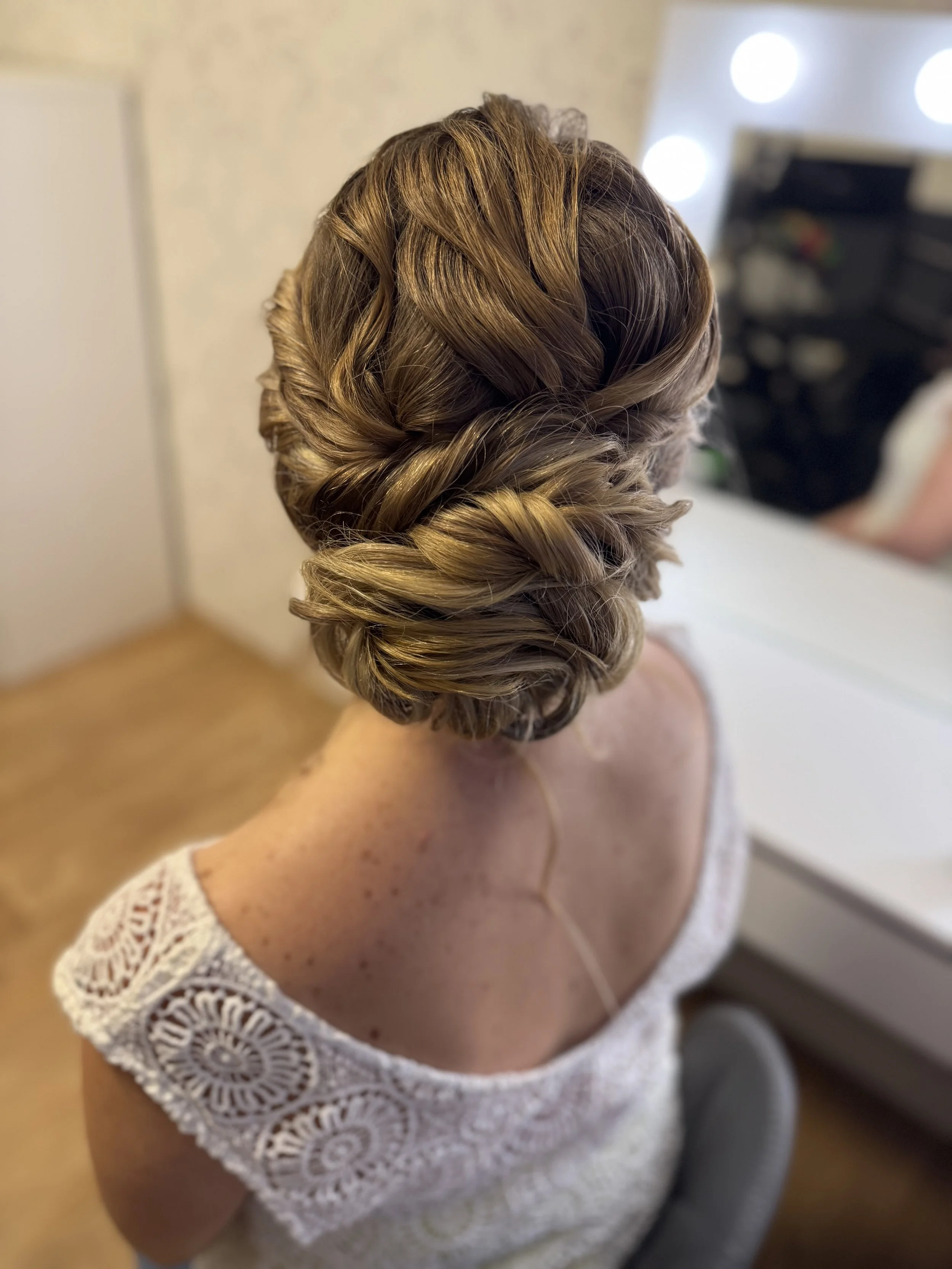 Coiffure élaborée avec des boucles élégantes dans les cheveux d'une femme portant une robe blanche en dentelle avec des manches en crochet.