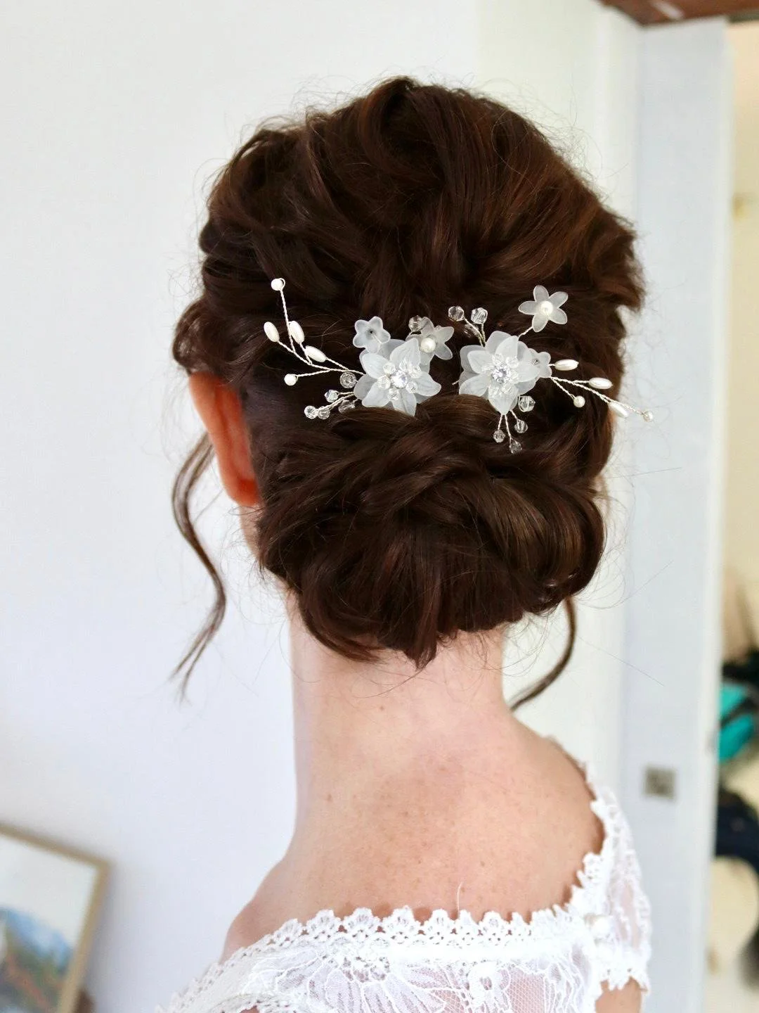 Coiffure de mariage avec un chignon bun orné d'un accessoire floral blanc avec perles et cristaux.