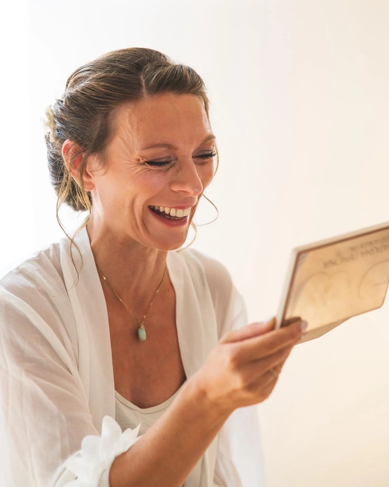 Une femme souriante regarde un livre ou un document qu'elle tient dans sa main.