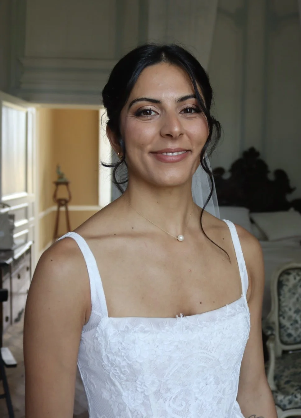 Femme souriante portant une robe blanche de mariée, dans une pièce lumineuse et élégante.