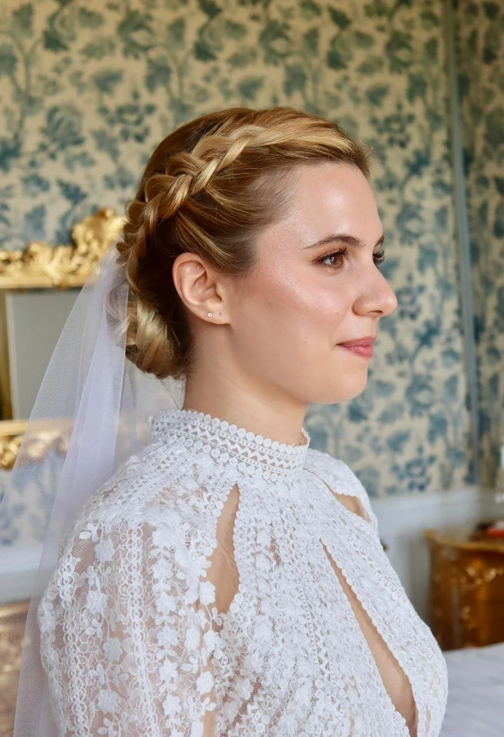 Une jeune femme en robe de mariée blanche avec un voile, coiffée d'une tresse, regarde vers la droite.