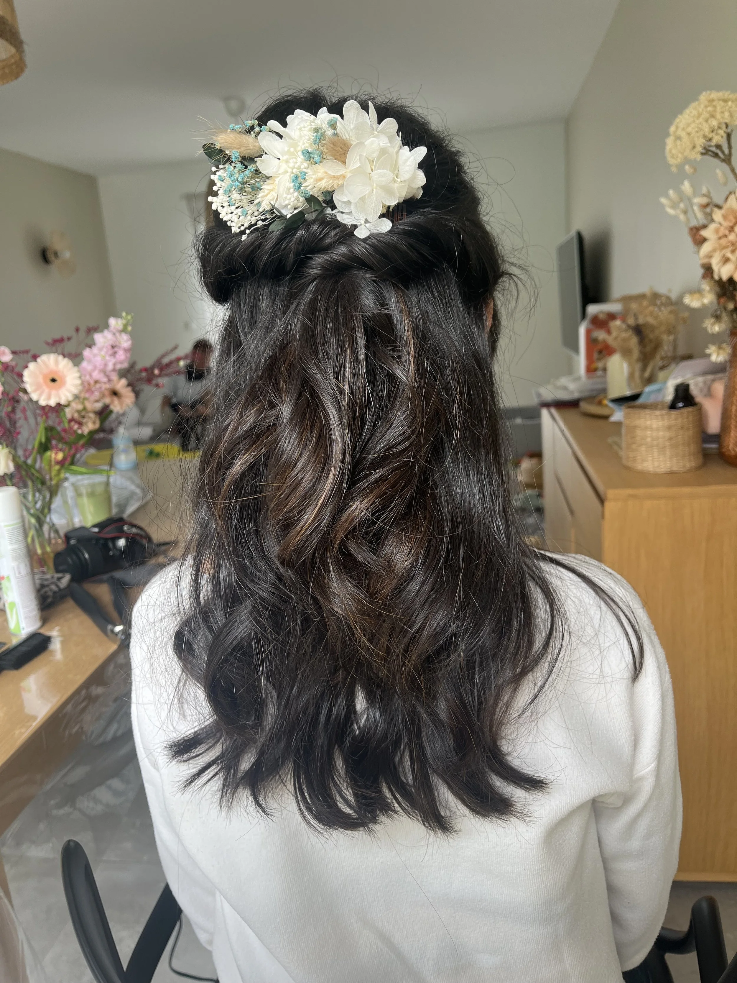 Coiffure avec cheveux mi-longs, vagues, et une coiffure relevée avec un accessoire floral blanc et bleu.