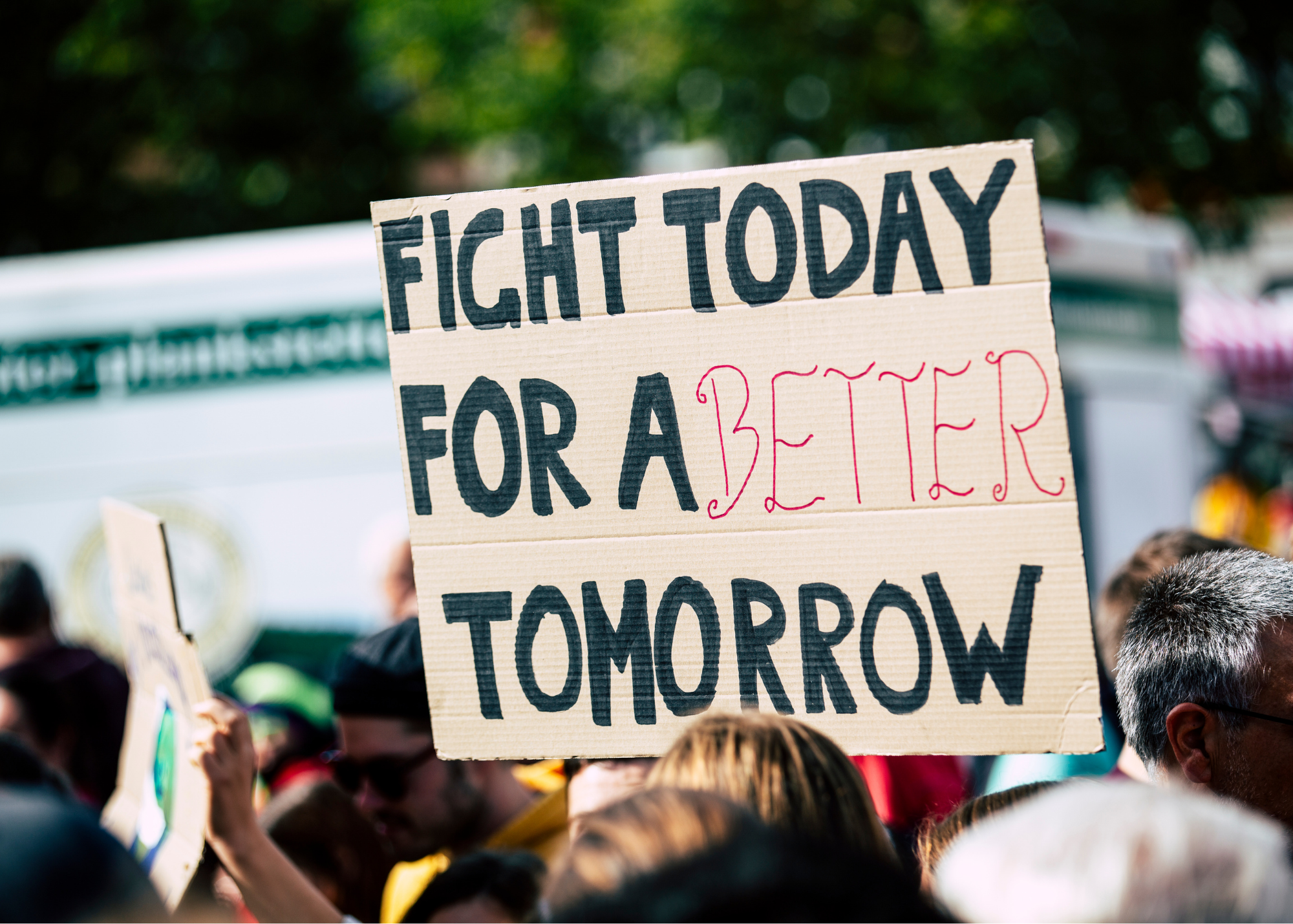 A crowd of people at a protest holding signs, with one prominently displaying the message 'FIGHT TODAY FOR A BETTER TOMORROW'.