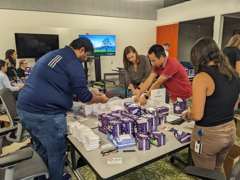 People organizing and packaging medical supplies, including boxes of gloves and masks, at a conference room table.