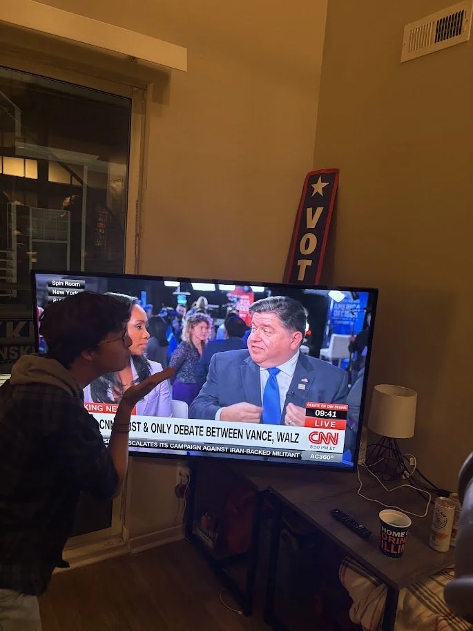 A student watching Governor J.B. Pritzker on television, gesturing as if to blow him a kiss.